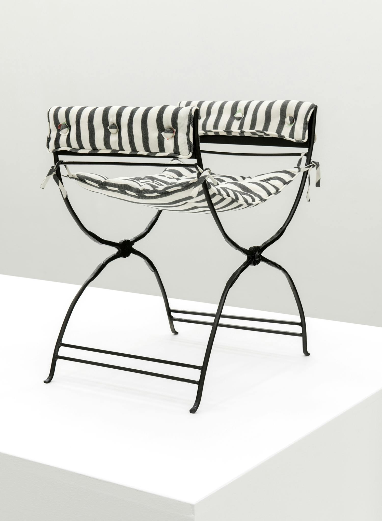 A black stool with black and white striped upholstery sits on top of a plinth. The fabric is made out of hand-woven silk.