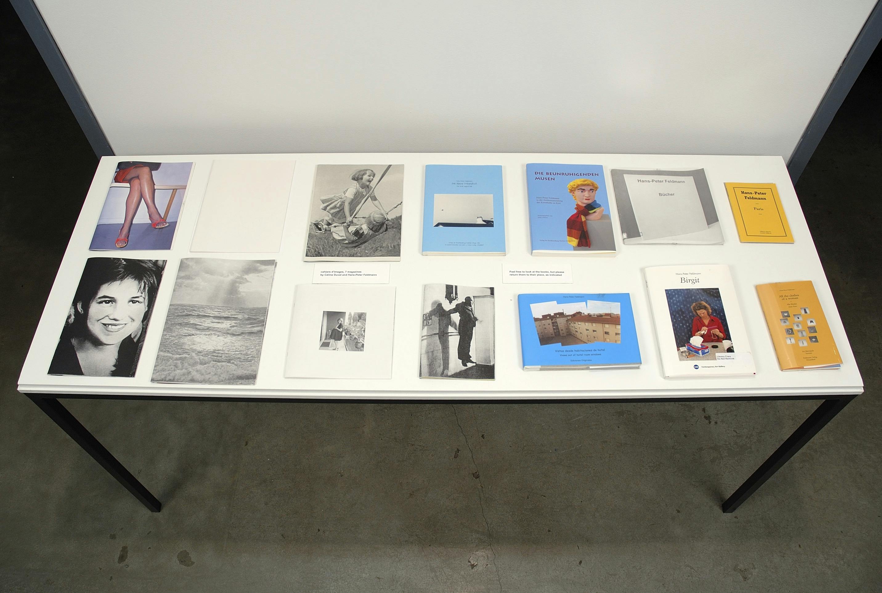 Several books displayed on a white table. The photos on the covers include two children laughing on a swing, legs of a person wearing heels and tights, and a person levitating in a room.
