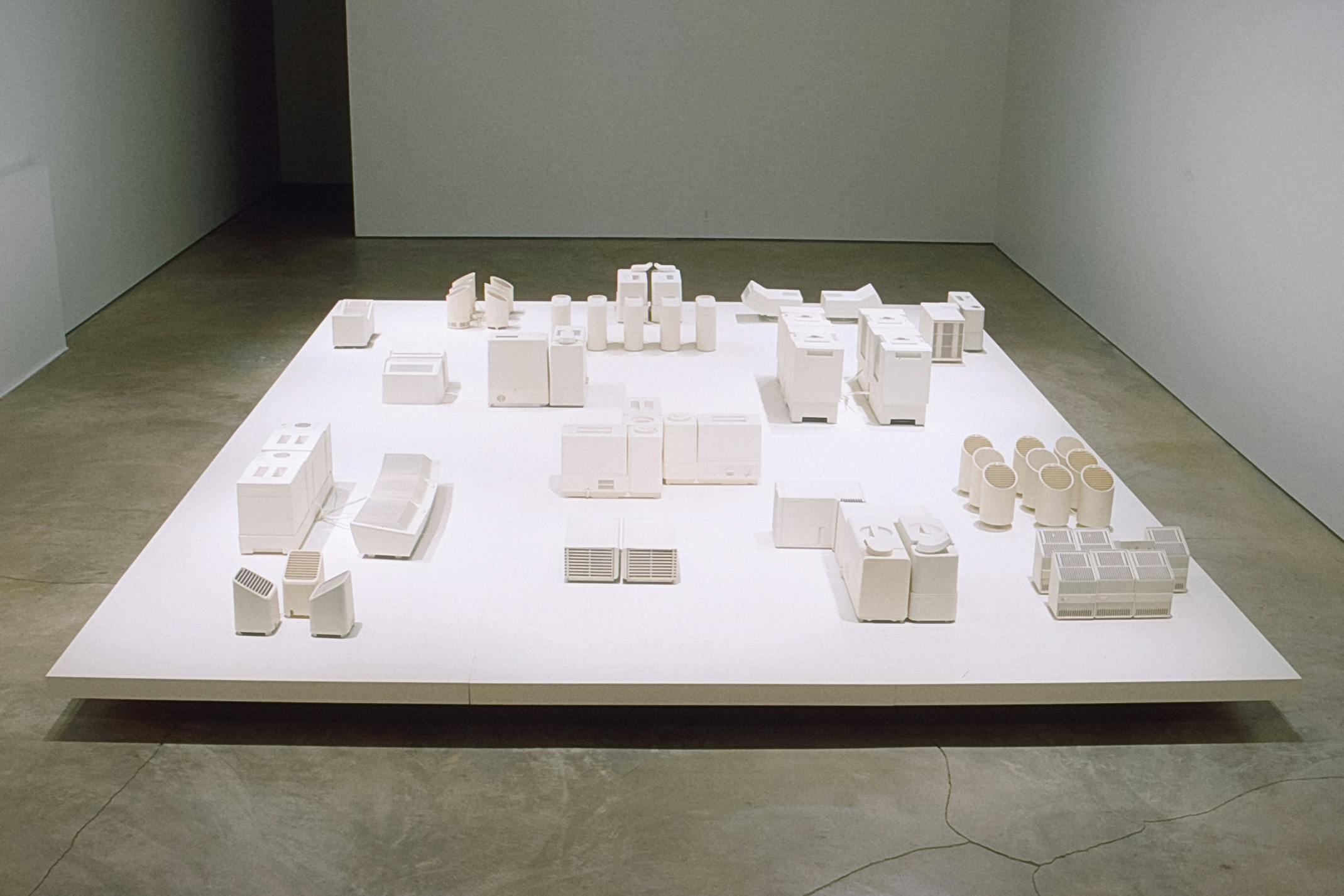 More than sixty white miniatures of electrics are placed on the white square panel on the gallery floor. They are the models of clean-mist humidifiers and negative-air ionizers. 