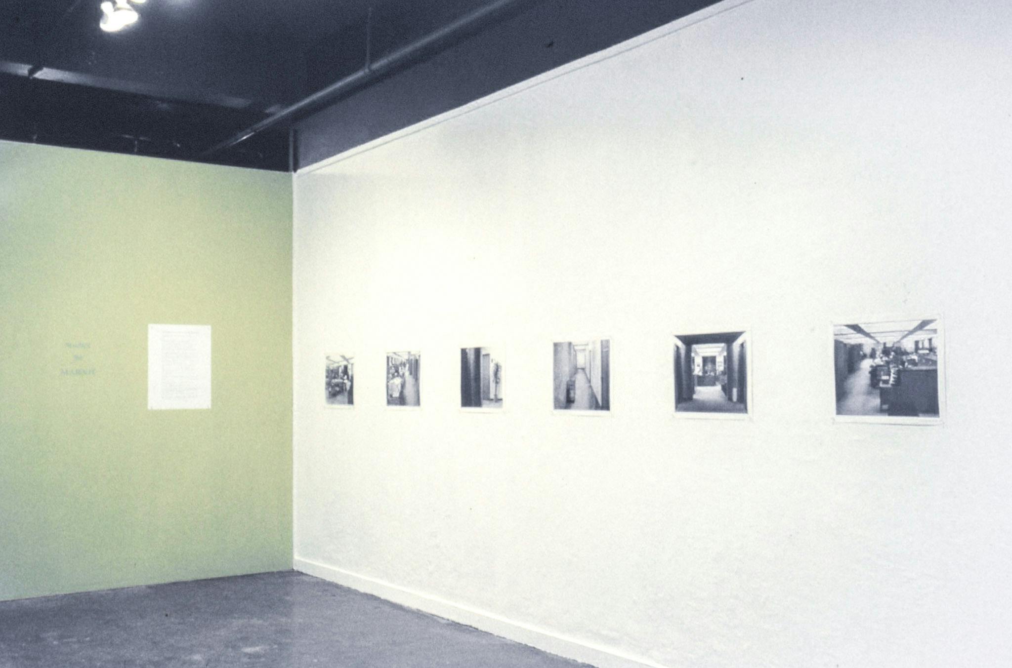 The corner of a gallery. One wall is white and shows 6 black and white images of architectural spaces, referencing the Hitchcock film, Marnie. The other wall is pale green and shows a sheet of text.