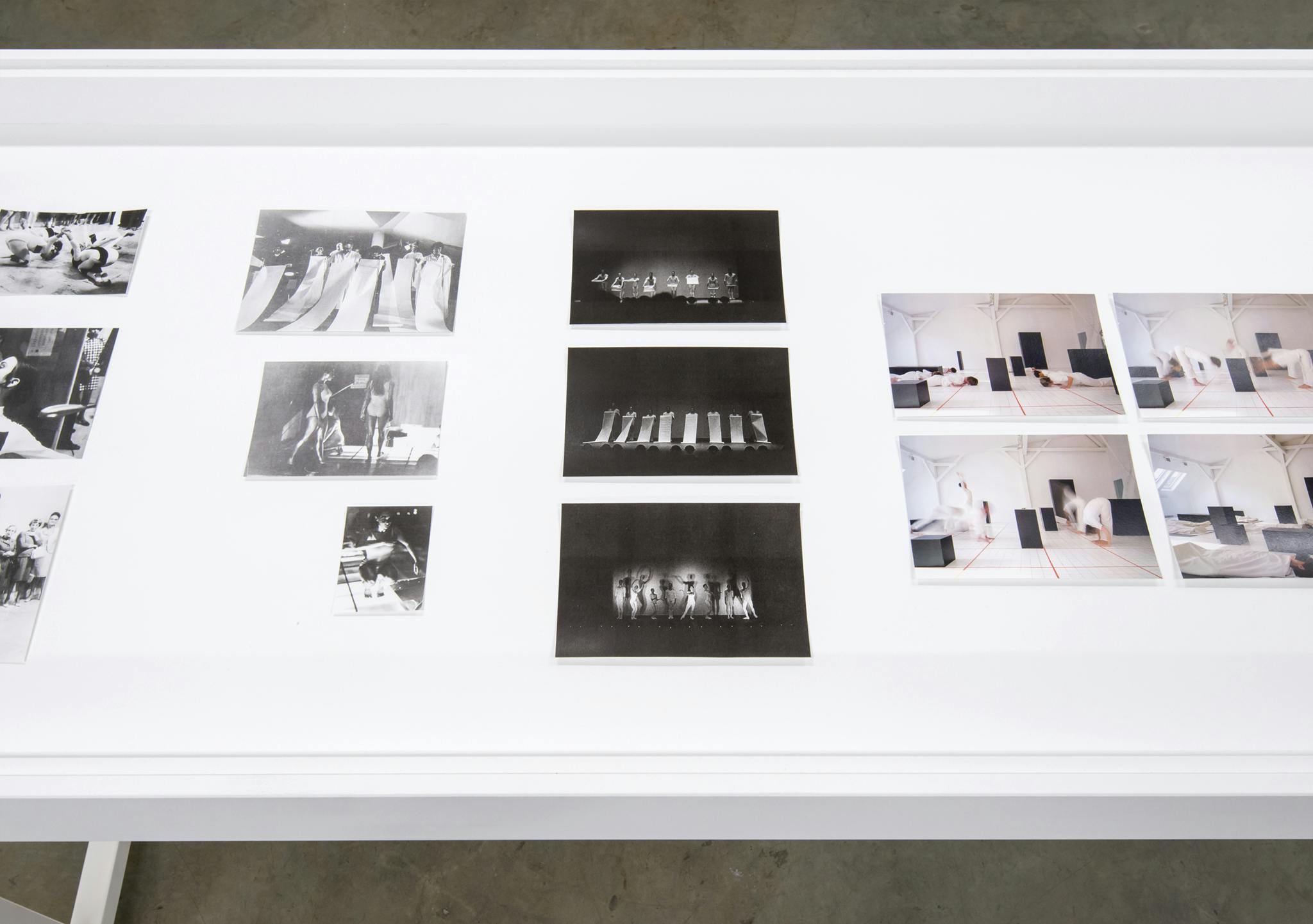 A detail image of the work of Channa Horwitz on a display vitrine. The thirteen photos are laid out in groups of three or four. The photos show groups of people in black in white and in colour.