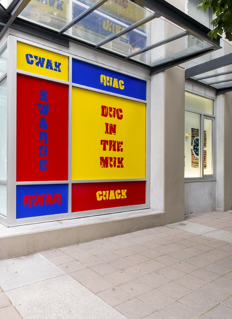 Kay Rosen’s work is installed on CAG’s exterior facade. Red, blue, and yellow vinyl sheets cover each panel of a window. Letters such as CWAK, QUAC, and KWAQUE appear in each panel.