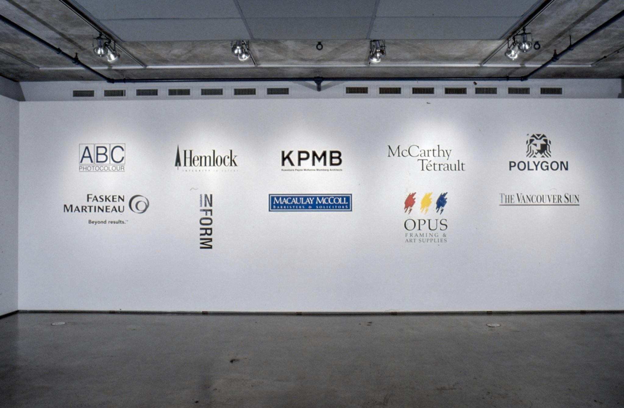 This is an installation shot of a gallery space. There are ten large-sized logos of different companies and organisations printed on a gallery wall.
