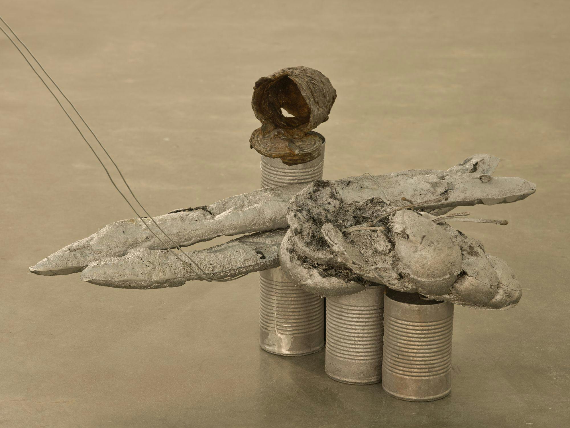 A detail of a sculpture comprised of silver-painted baguettes, wire, aluminum cans and a bronze can.