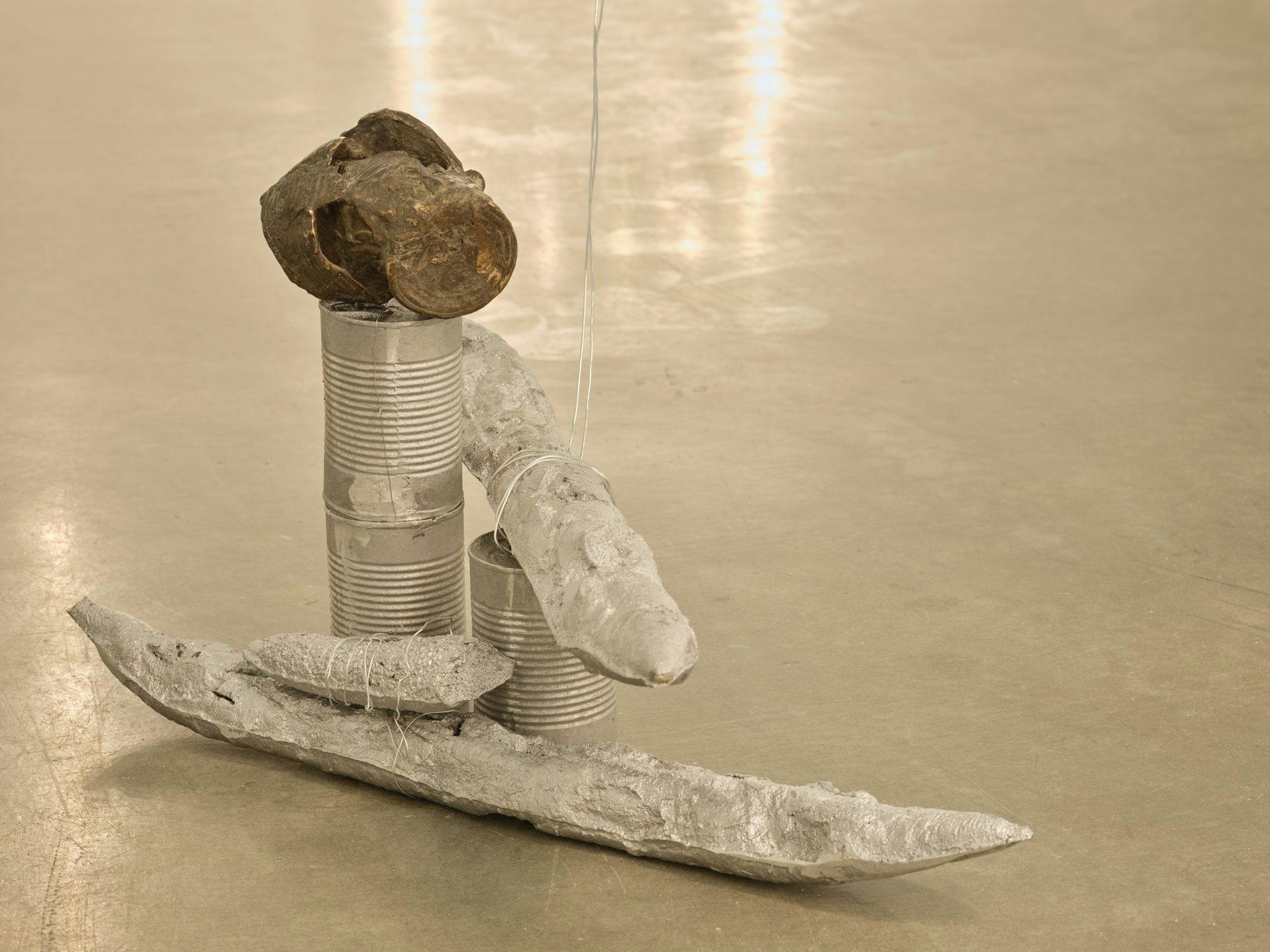 A detail of a sculpture comprised of silver-painted baguettes, wire, aluminum cans and a bronze can whose form appears to be disintegrating.