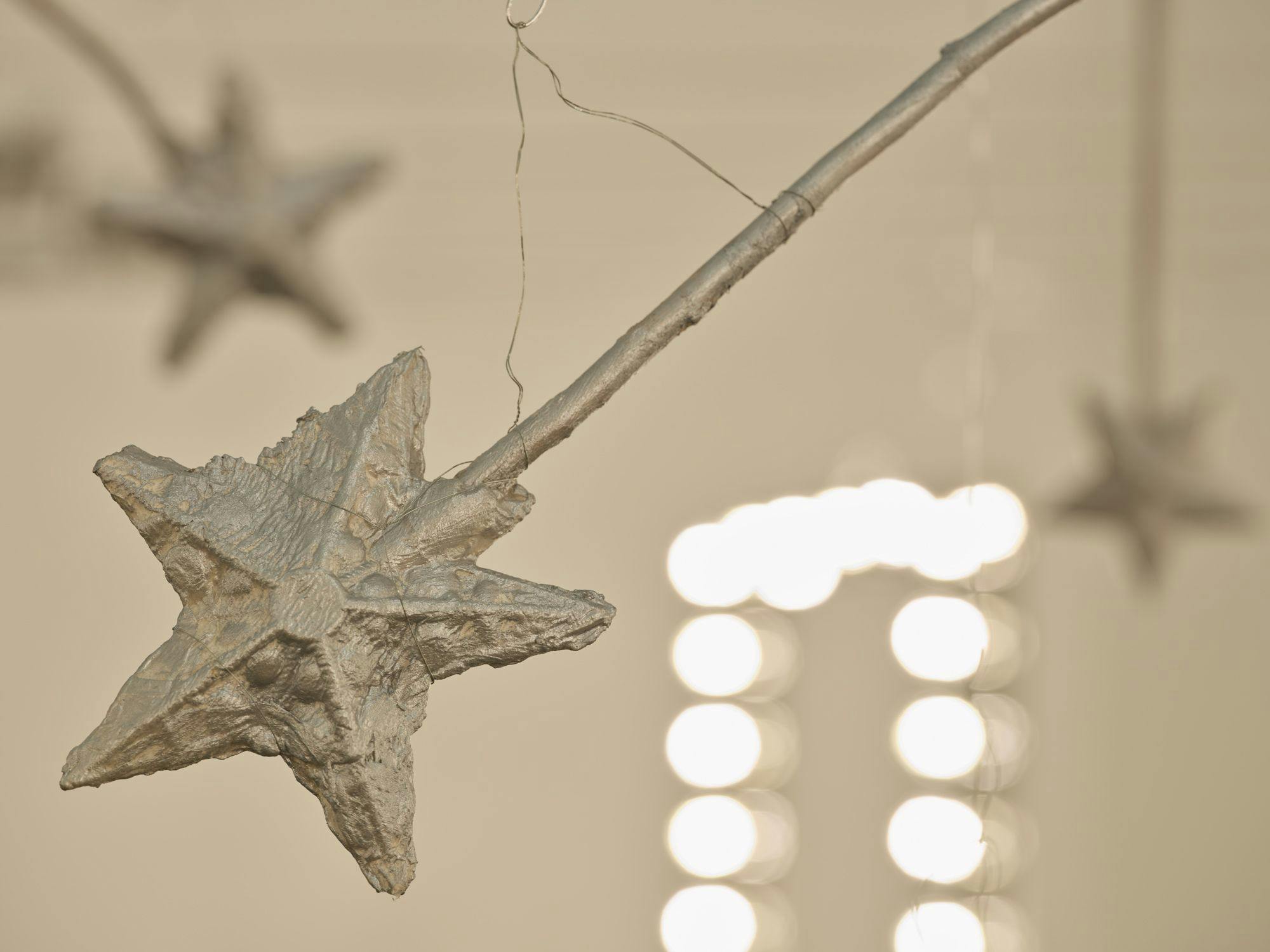 A detail view of a silver magic wand. In the background are a vanity light and more magic wands hanging from wire.