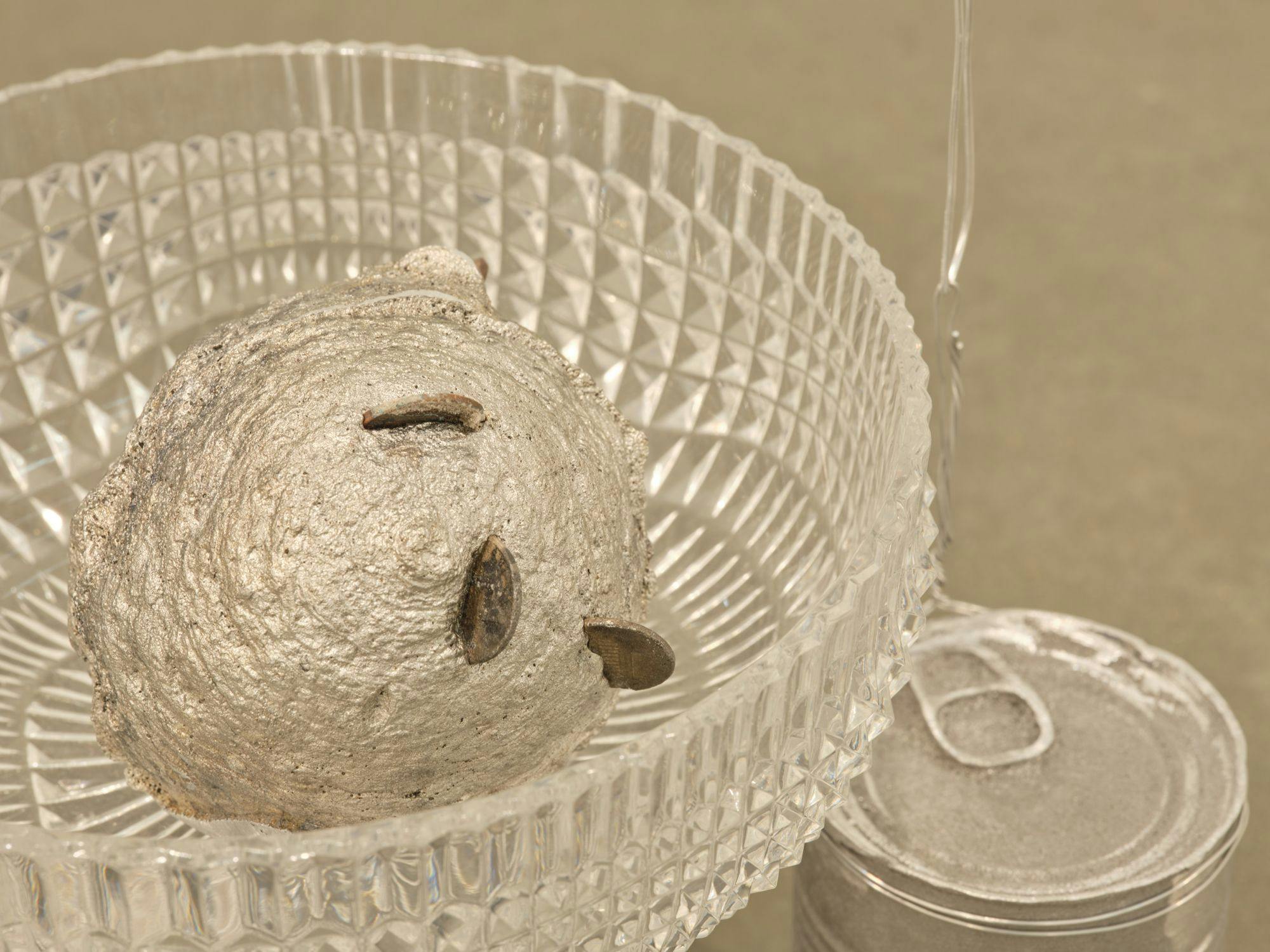 A detail of a sculpture comprised of glass bowls, wire, aluminum cans, and a ball with copper coins sticking out.