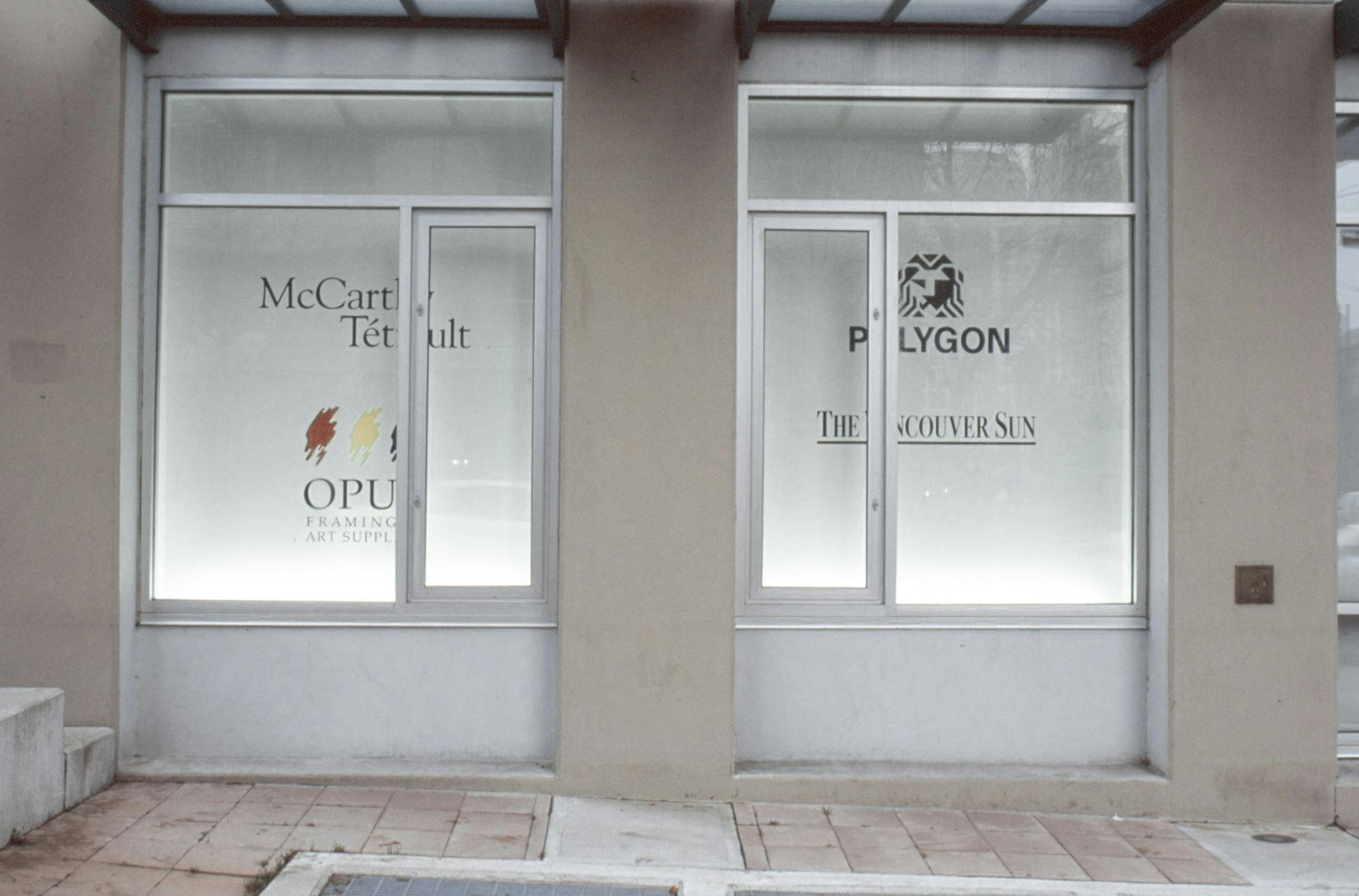 Two of the CAG window spaces are visible in this photograph. Four logos of different companies and organisations are printed on the white walls behind the windows. 
