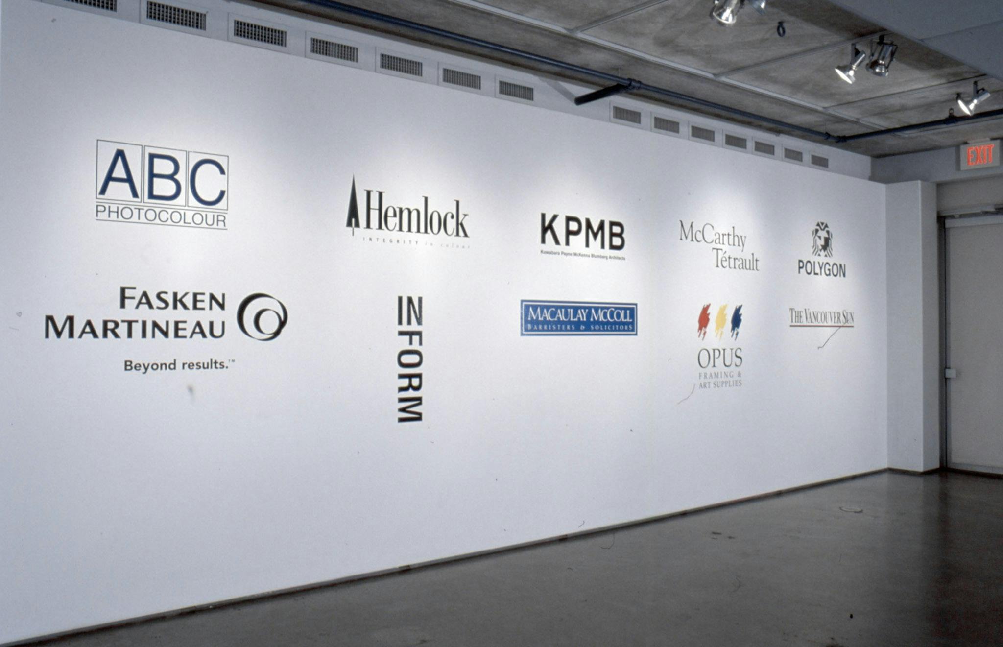 This is an installation shot of a gallery space. There are ten large logos of different companies and organisations printed on a gallery wall.