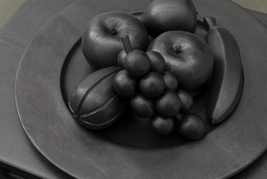 Detail image of fruits on a plate carved out of wood. The entire sculpture is coloured black.