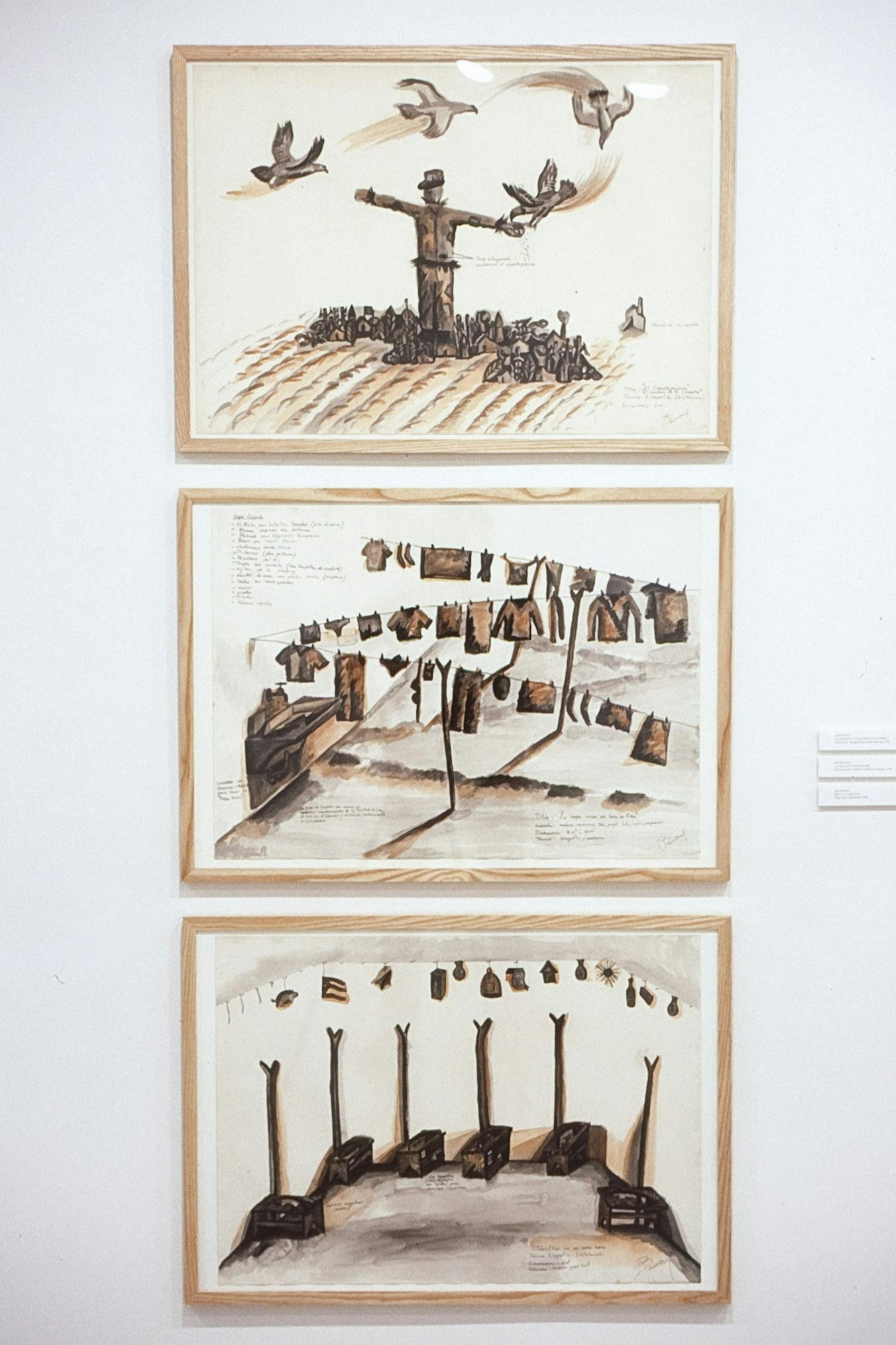 A set of three drawings are vertically aligned on the gallery wall. The top image shows a large scarecrow standing in the middle of the village. The middle piece shows clothes being hung to be dried. 
