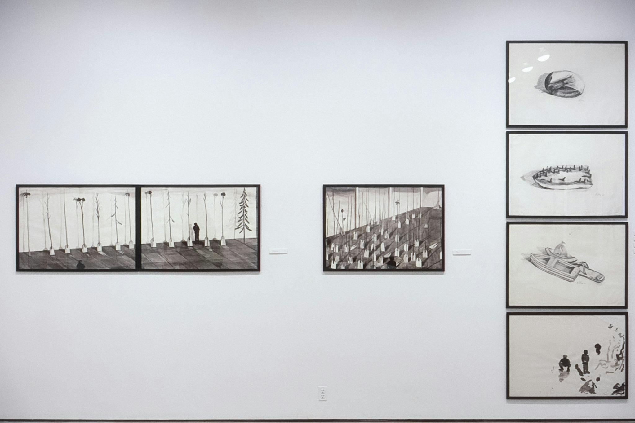 Seven black and white drawings are installed on the gallery wall. Many of them include small shadows of humans and boats. Three of them line up horizontally and the rest line up vertically. 