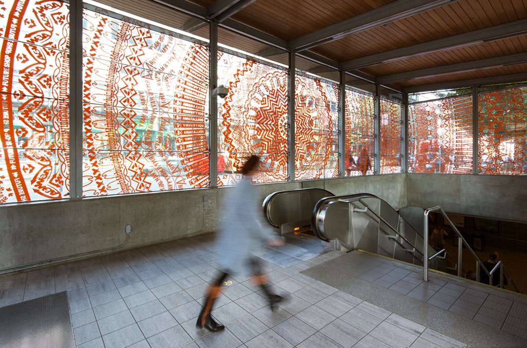Image of Gunilla Klingberg’s work installed at Yaletown-Roundhouse Station. An orange mandala-like pattern in vinyl covers the large glass windows of the station’s facade.