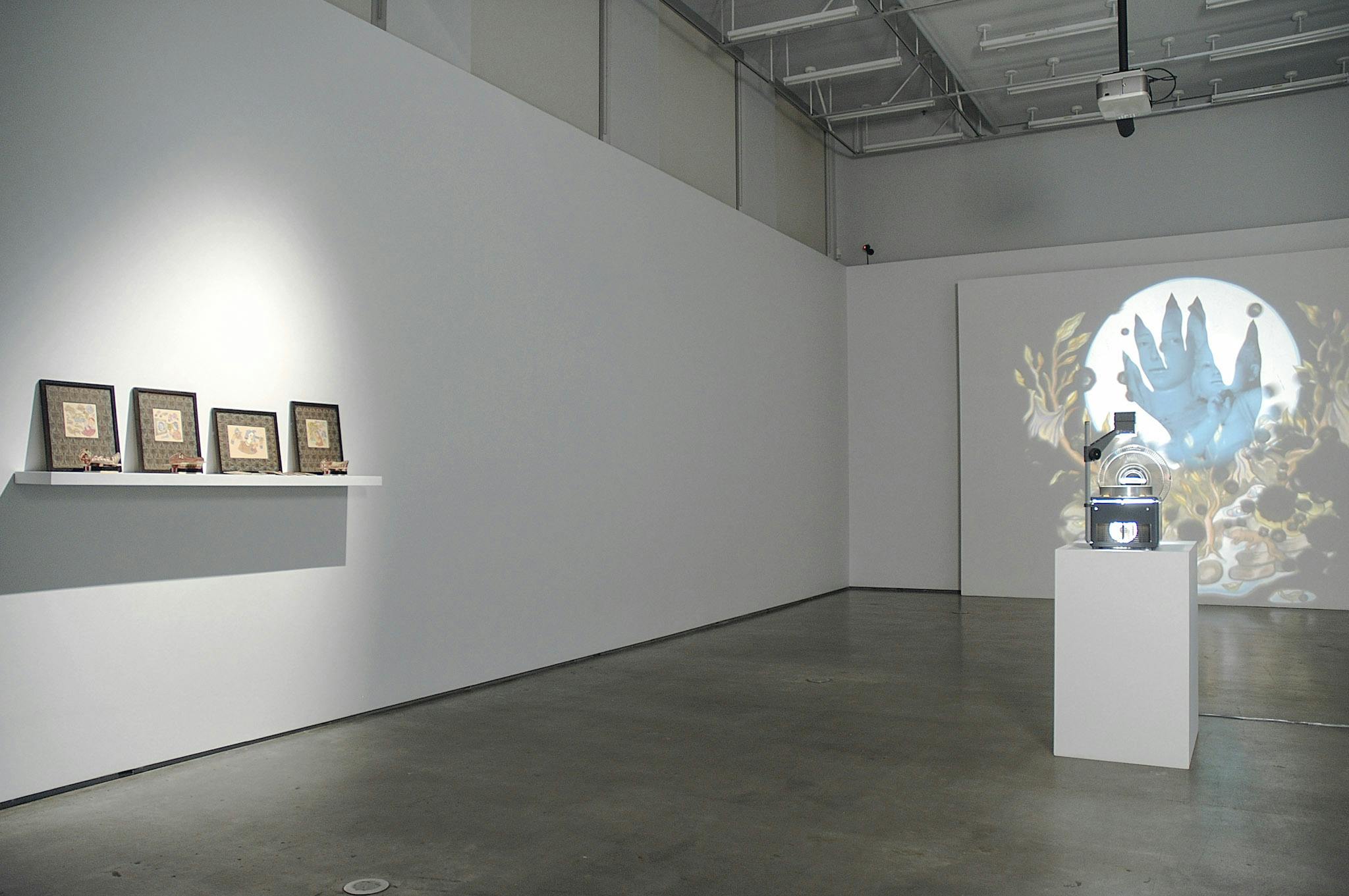 An installation image of artworks in a gallery. Four framed illustrations are placed on a small shelf attached to a wall on the left side. A projector placed in the middle of the room project an illustration of a blue hand on a far wall.