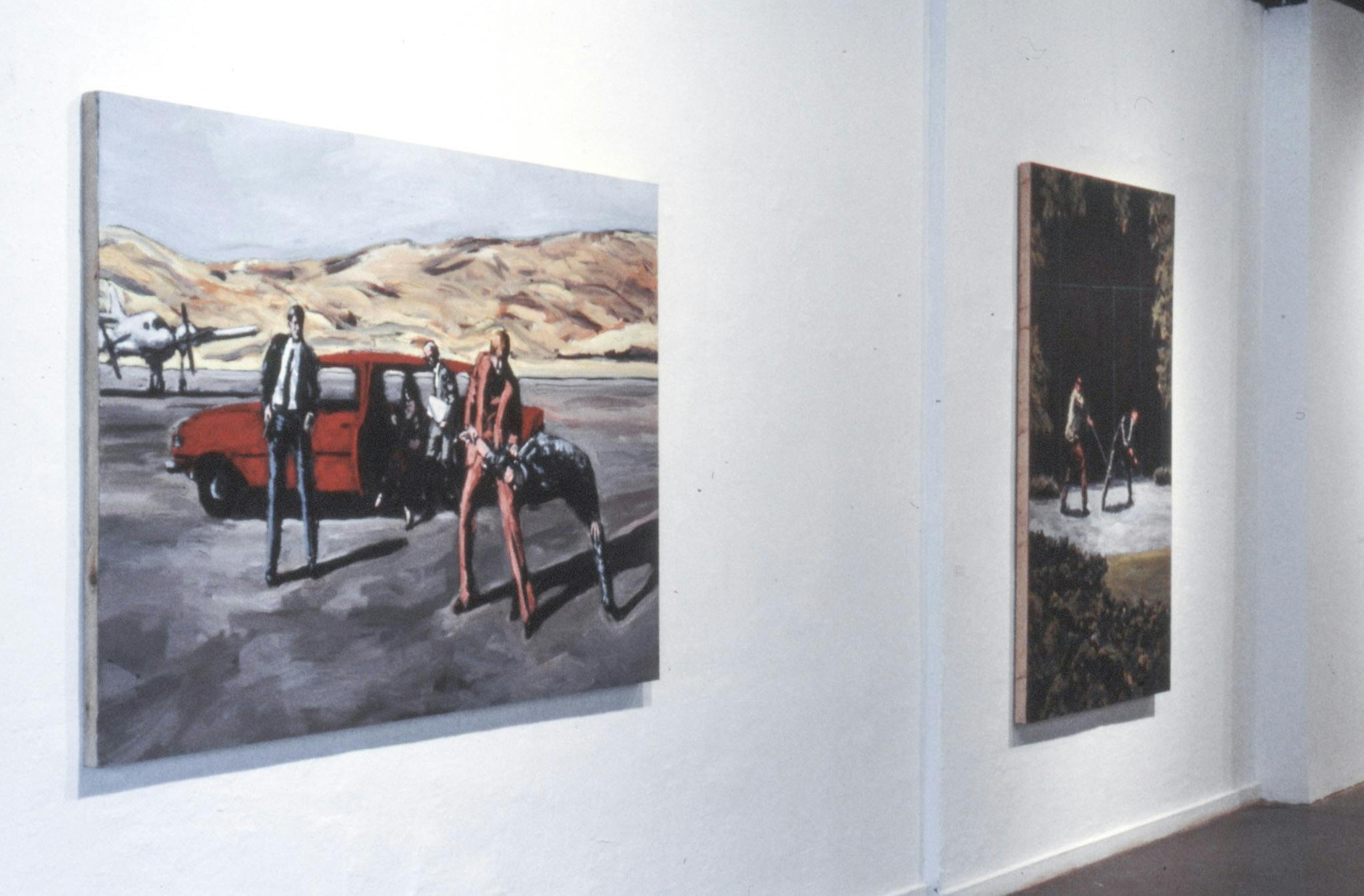 A closeup of 2 large paintings on a gallery wall, both showing different scenes. One shows 5 people in and around a red car on an airport landing strip. The other shows 2 people in a dark wooded area. 