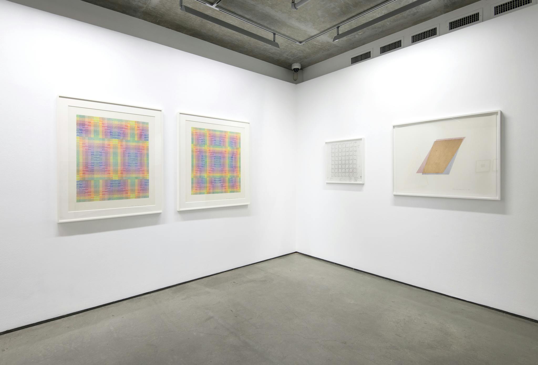 Four framed drawings hang on the walls of a gallery. Three drawings are of a grid, two of them are large colourful and vibrant, one is a small simple sketch. The fourth drawing is of a parallelogram.