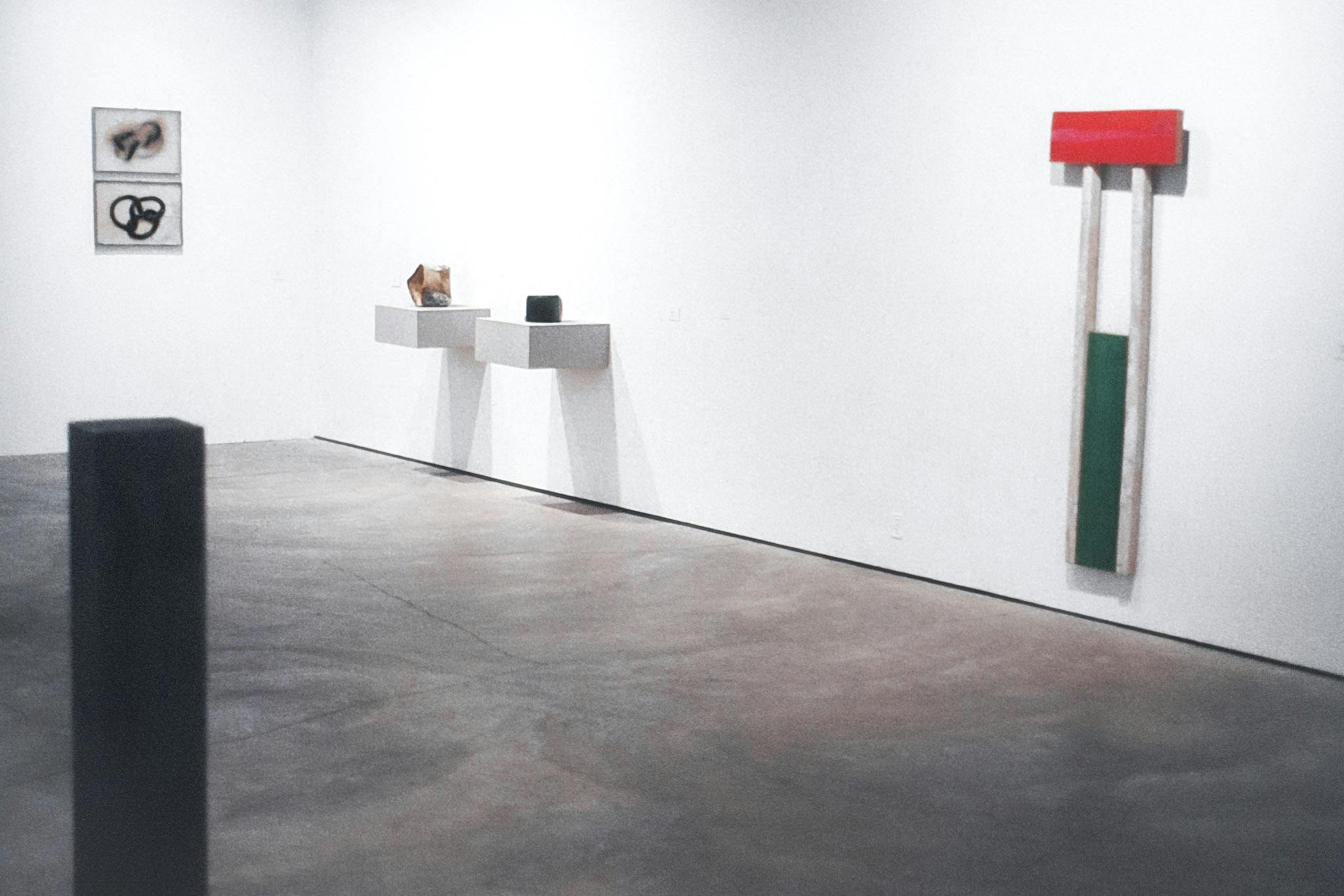 A gallery space with many artworks. Two of the works are on plinths on the wall, and 2 others are directly mounted. In the corner of the image, there is a work that is a large white rectangular prism.