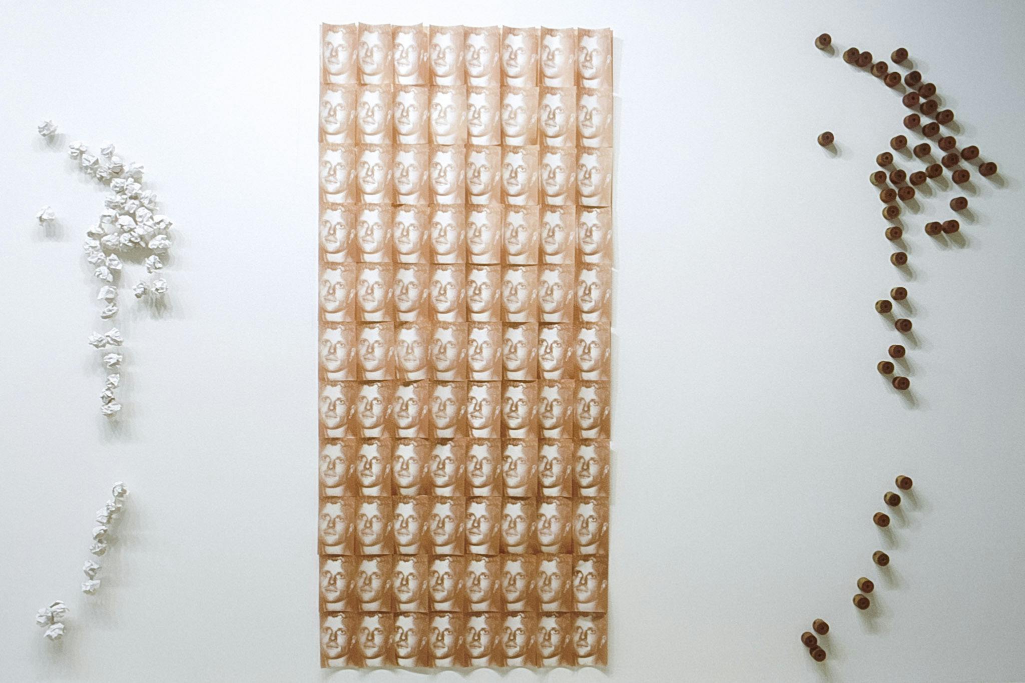 Identical images of a man’s face are installed on the gallery wall. In total 88 of those images, printed in orange-brown and closely aligned to each other, resembles a chocolate bar. 