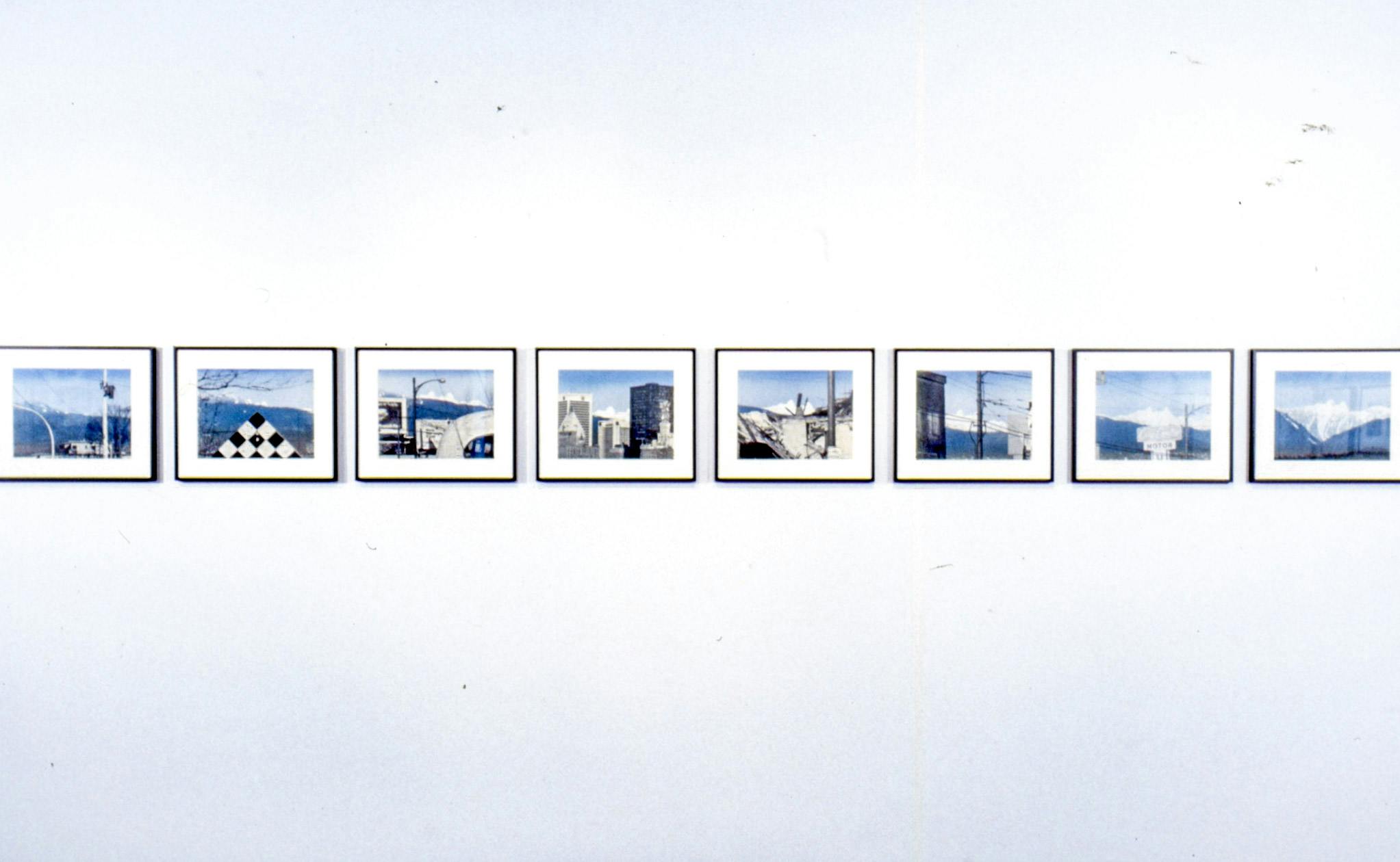 A set of eight coloured drawings are mounted on the wall. Those images are dominated by blue, grey, and white. These depict different scenes of a city foregrounding blue mountains and the sky.