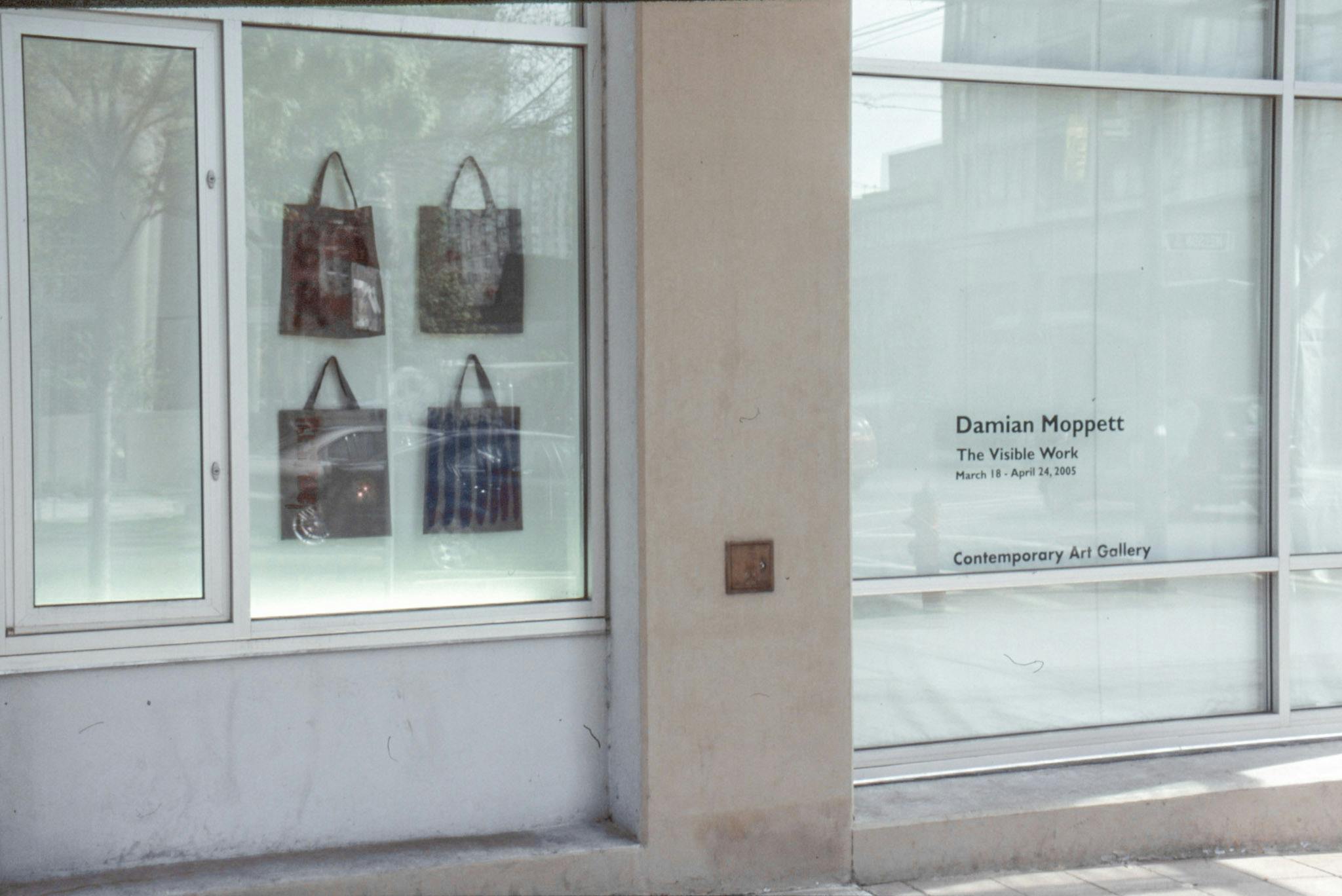 An install image of CAG’s window spaces facing Nelson Street. Four tote bags are mounted behind the glass. On the other window, the artist’s name and exhibition information are printed on vinyl.