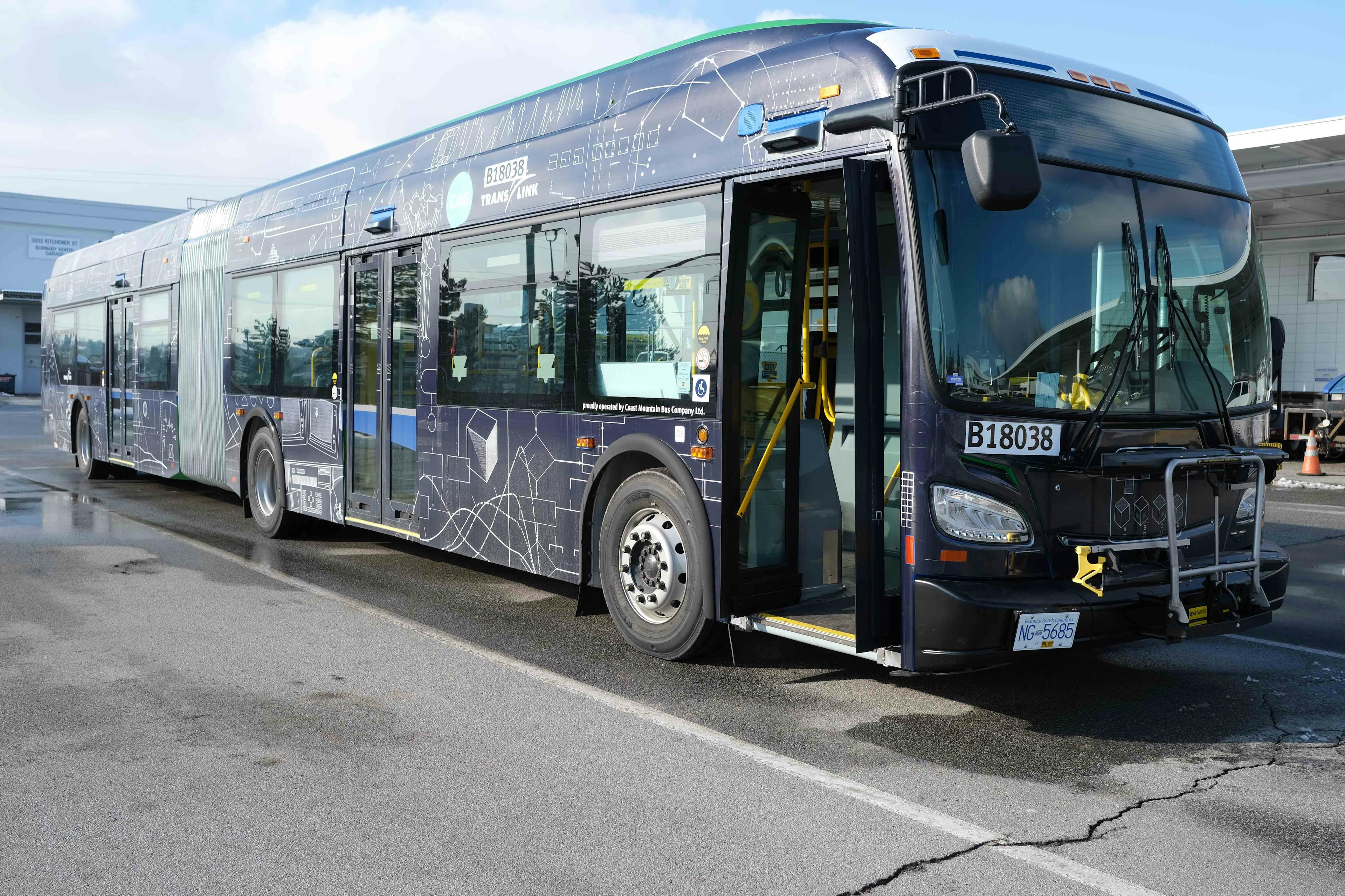 An image of the exterior of a transit bus wrapped in a patterned vinyl. The imagery on the vinyl resembles blueprint-like geometric shapes, composed of thin white lines on a dark blue background. 