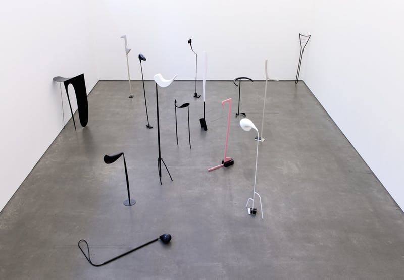 A series of tall, abstract sculptures by Nairy Baghramian installed in a gallery. Many of them, free-standing on the floor, appear to have long necks with thin heads. Their shapes resemble music notes. 