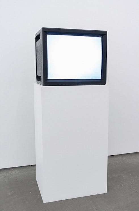 An installation view of a work titled Watercolour by Ceal Floyer. A CRT TV installed on a white pedestal displays a surface of a white screen.