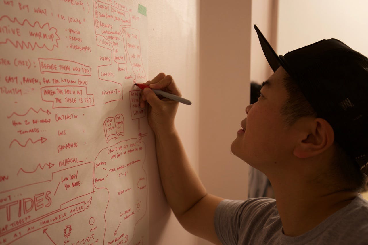 An image of a person writing texts on the whiteboard with a red marker. 