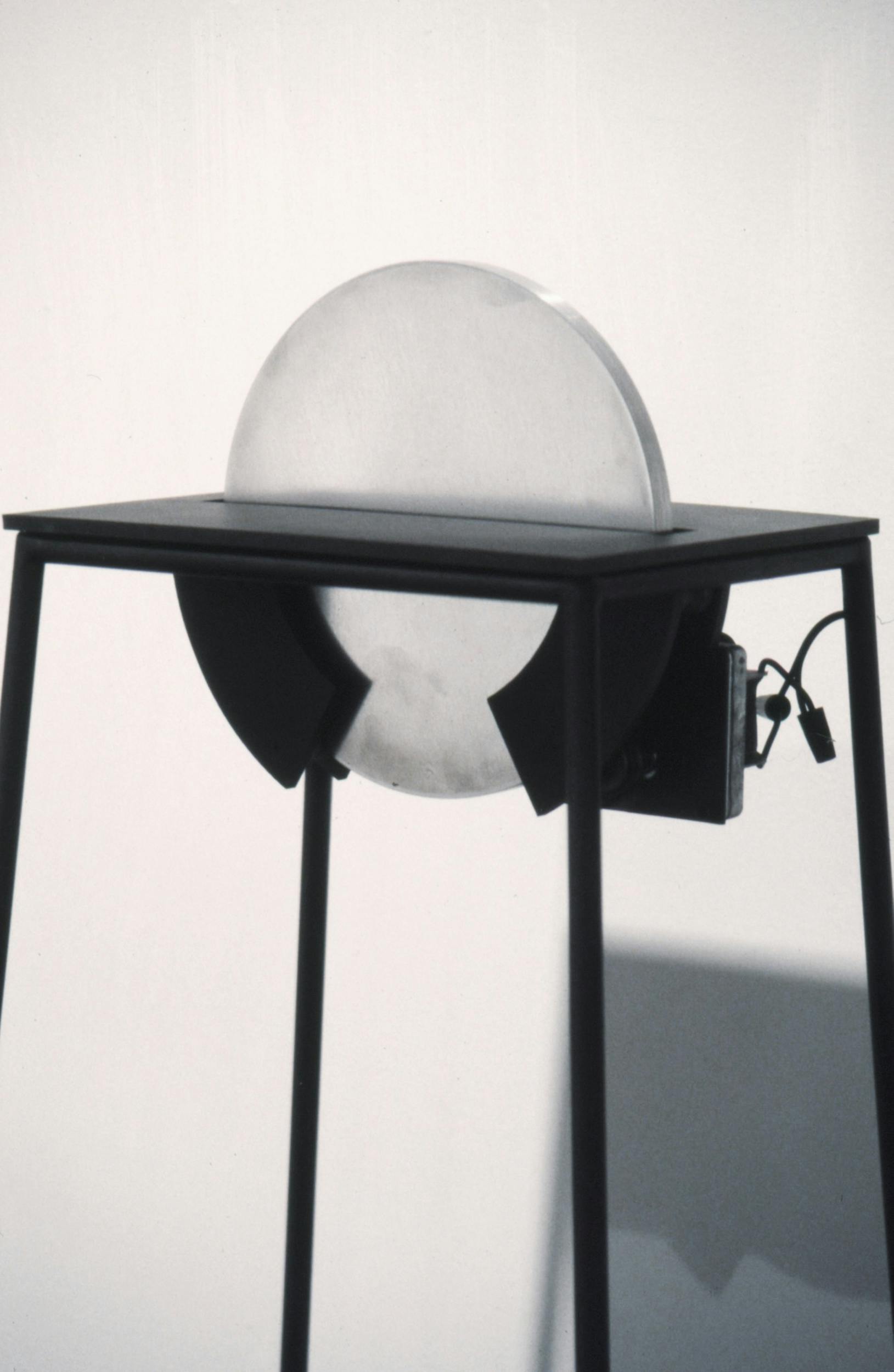 A close view of a sculpture in a gallery. The sculpture is made of a flat metal disk sitting upright in a black stand.