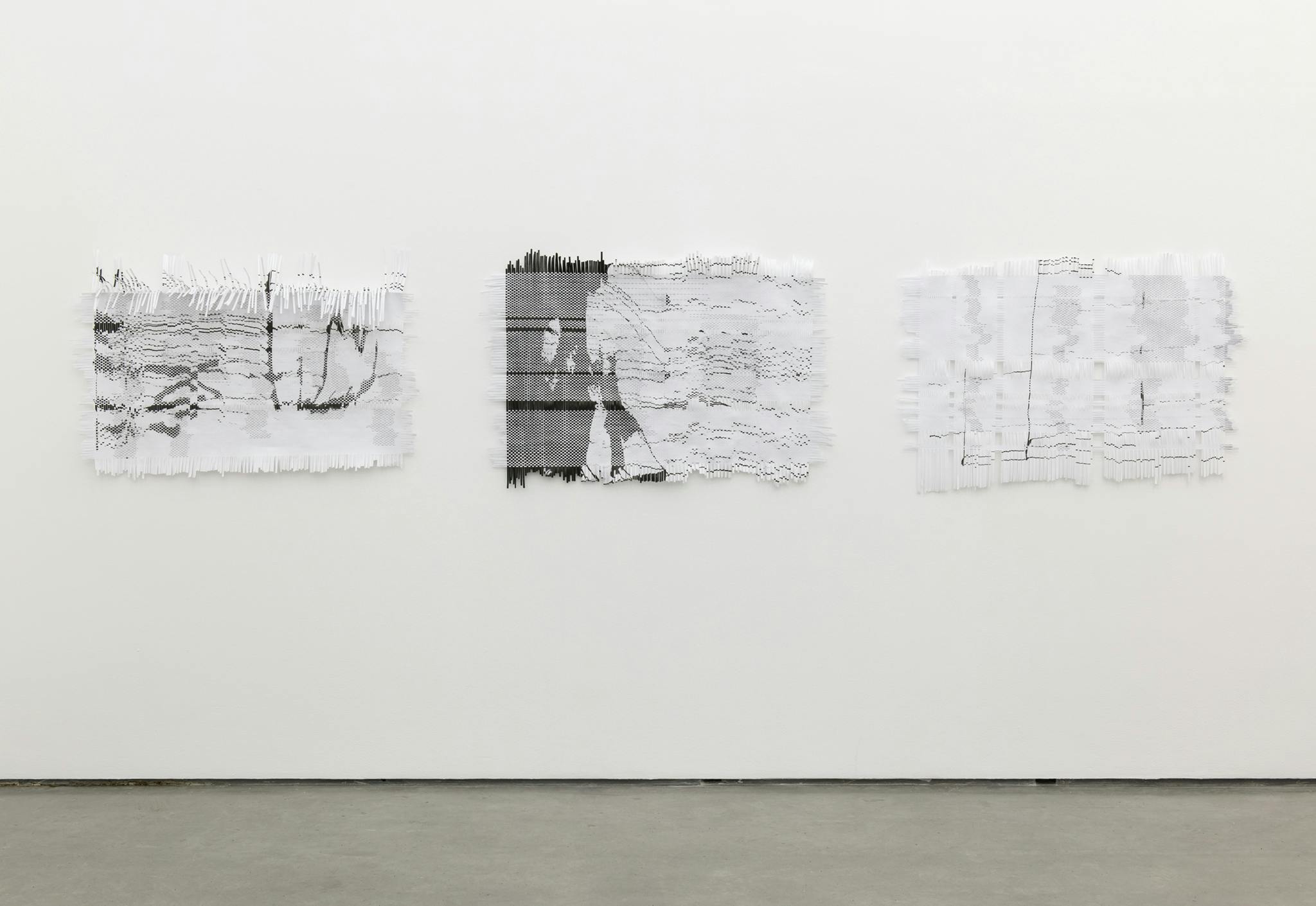 Three woven, rectangular artworks hang horizontally on the wall. The weavings are made of white paper printed with black marks. 