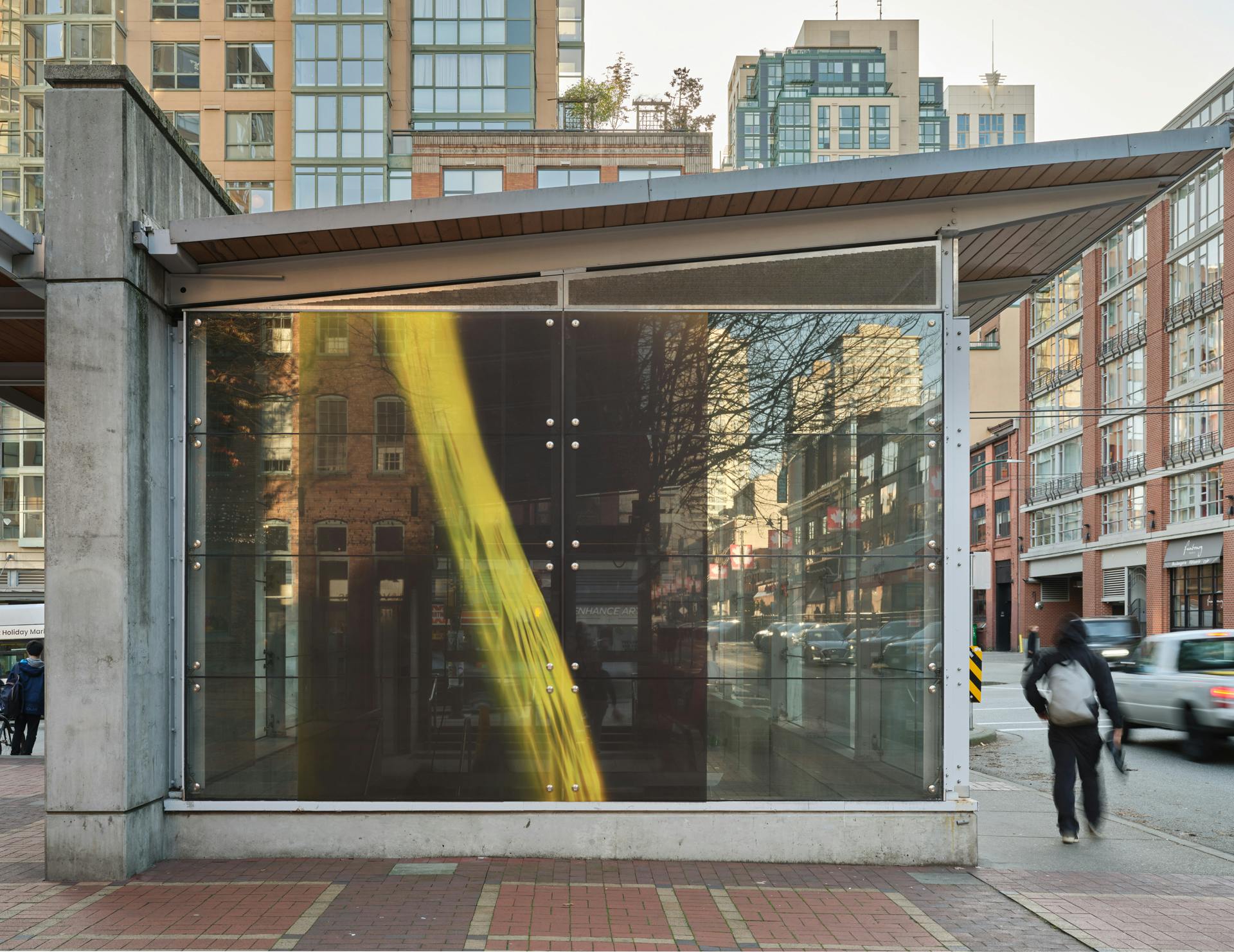 A frontal view of a SkyTrain station with one photogram in its window. The photogram depicts a yellow nylon produce bag against dark photographic paper.