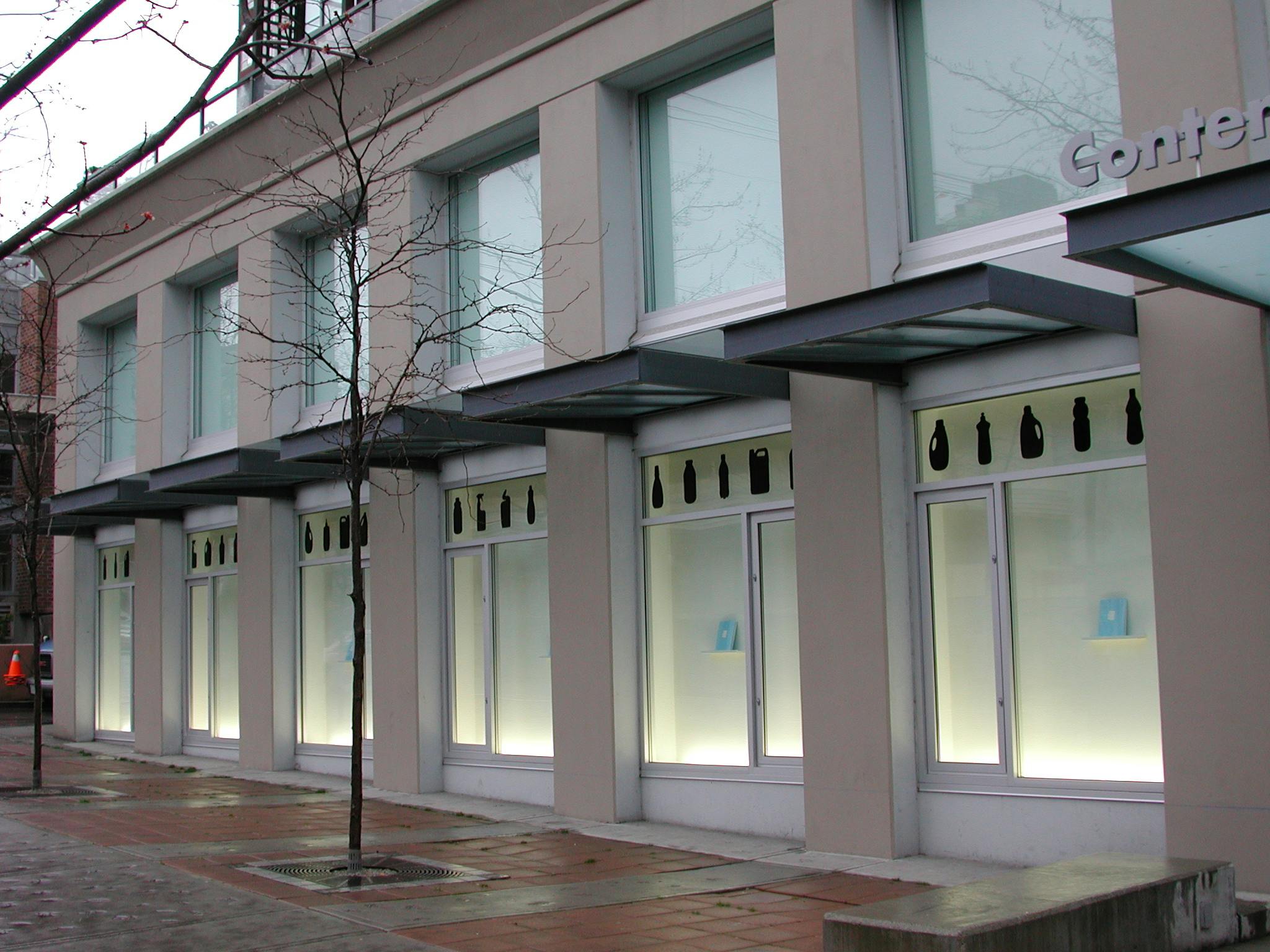 This is an installation shot of CAG’s building facade. Silhouettes of household objects such as cleaning sprays are printed at the top of the windows. Books are installed inside the window spaces.