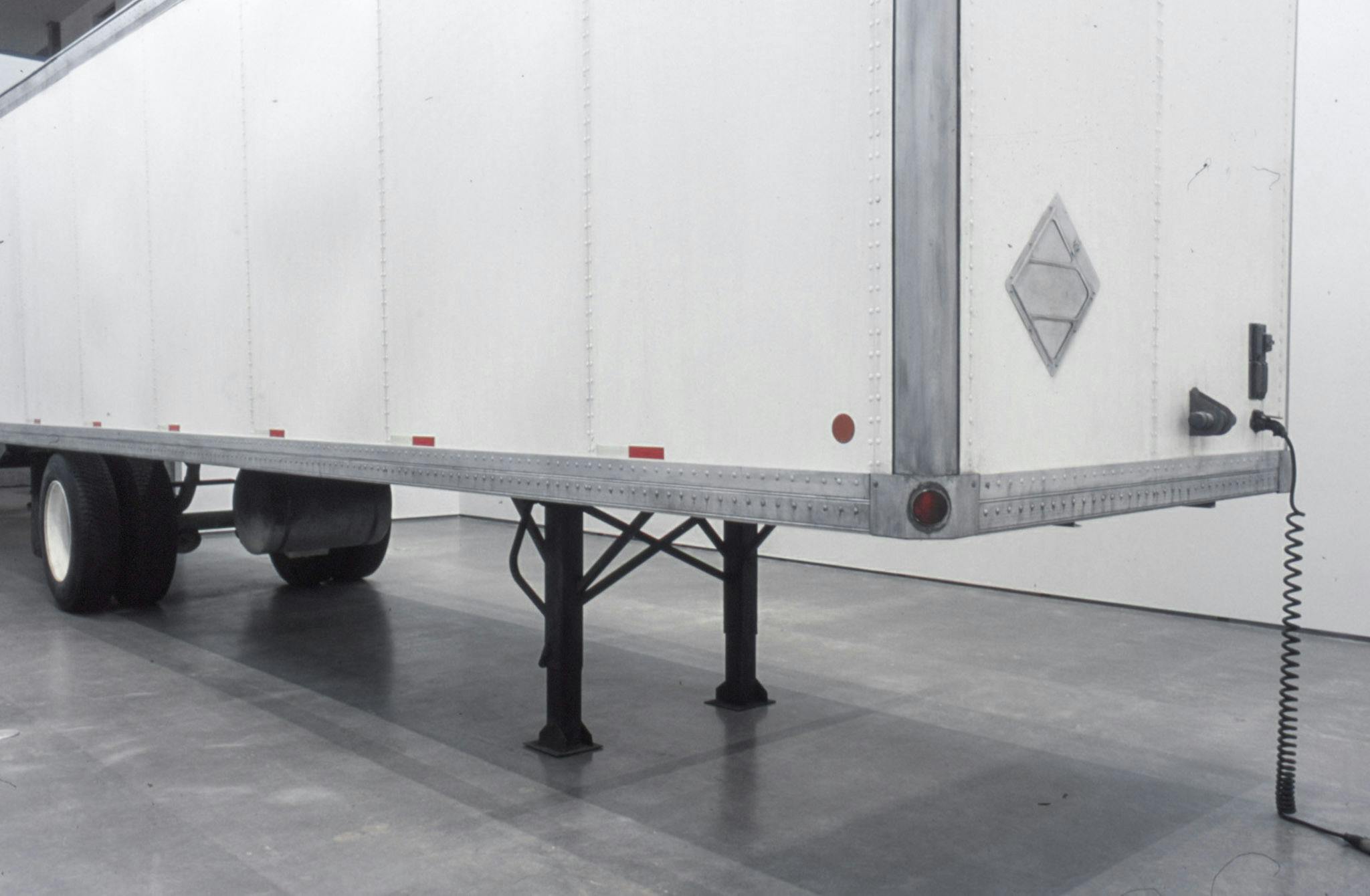 This is a close-up view of the sculptural installation by Geoffrey Farmer. A large white semi truck trailer sits in a gallery space. This image shows the front of the trailer.