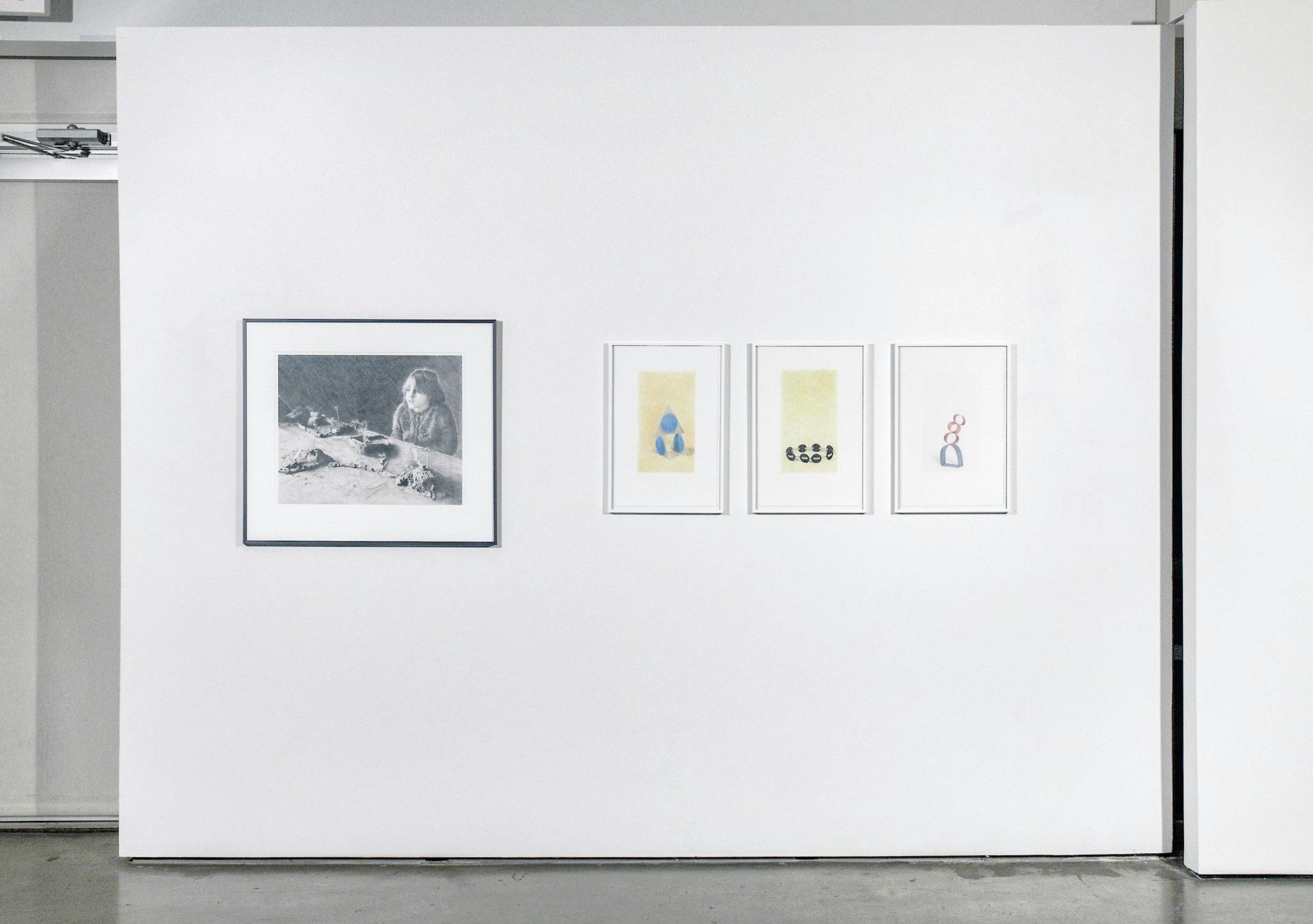Four drawings are mounted on a gallery wall. A set of three coloured drawings depict sculptures made of geometric shapes. There is also a black and white drawing of a child sitting at a table. 