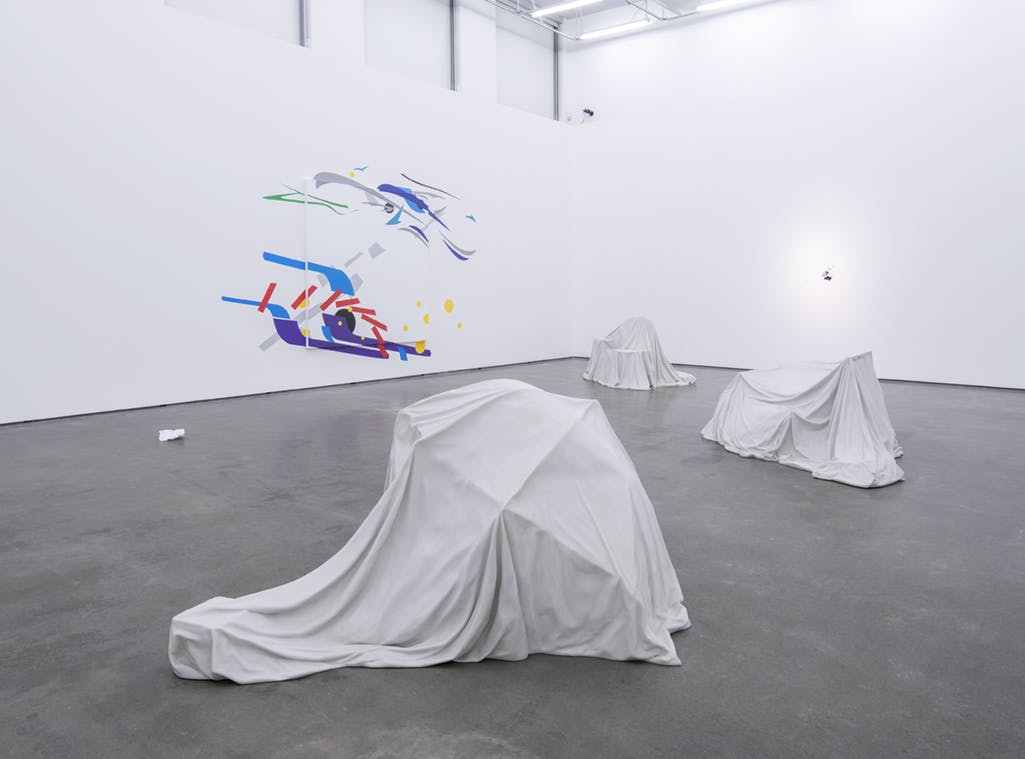 Three large-scale, marble sculptures resembling child-made forts of draped sheets, chairs, and other objects. Behind, a large-scale, abstract work of colourful geometric shapes is mounted on a wall.