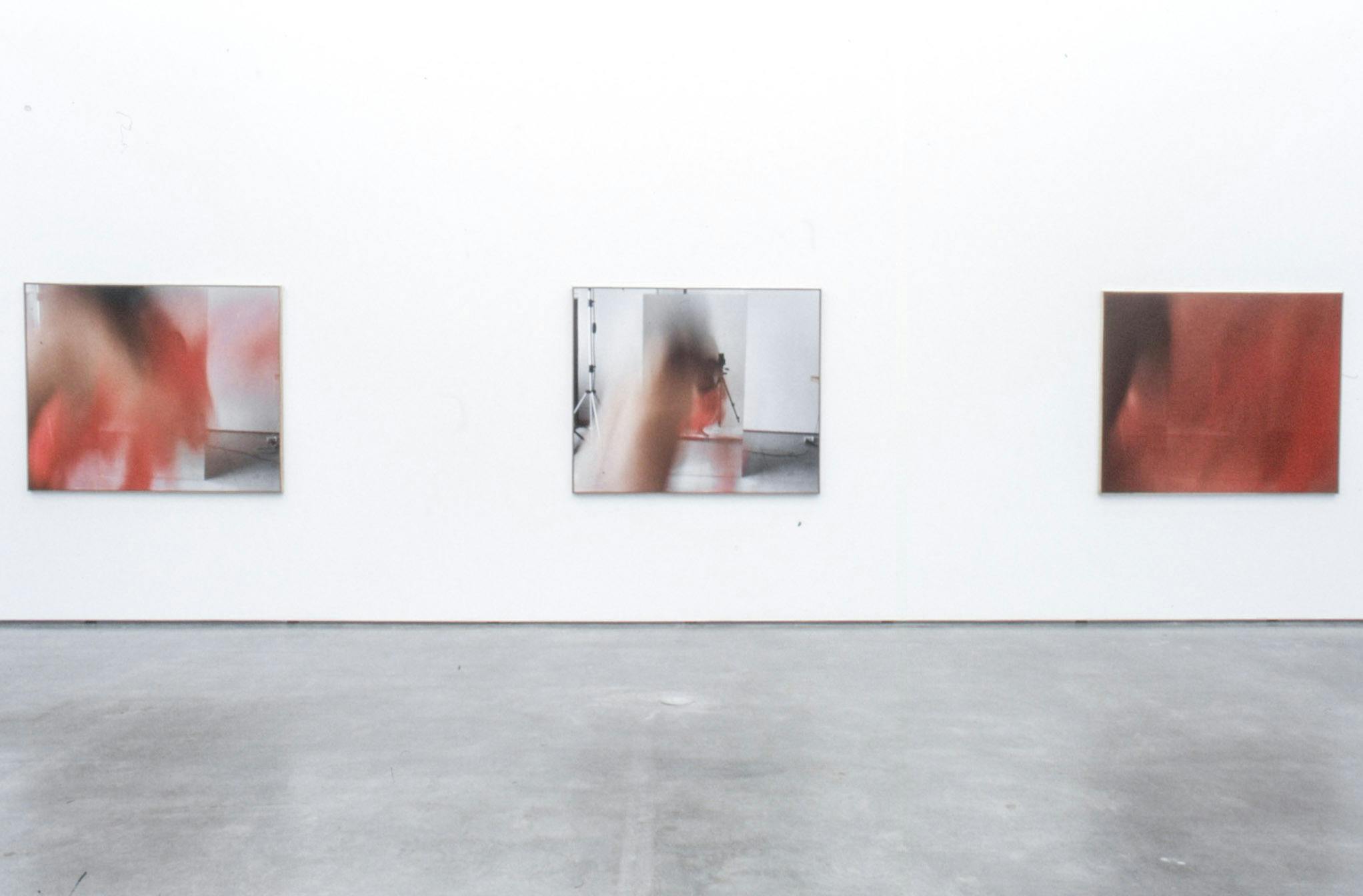 Large-sized photographs are installed on the gallery walls. Three photographs visible in this image all show blurred images of a person dancing with a piece of red-coloured fabric. 