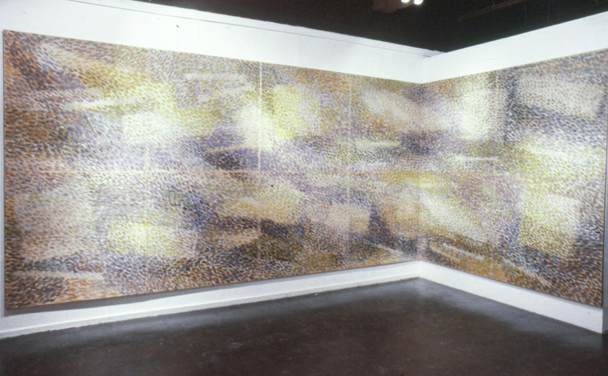A large painting takes up most of the two walls in the corner of a gallery. It is made of 12 different square plywood panels and painted with small colourful brushstrokes, reminiscent of a landscape.