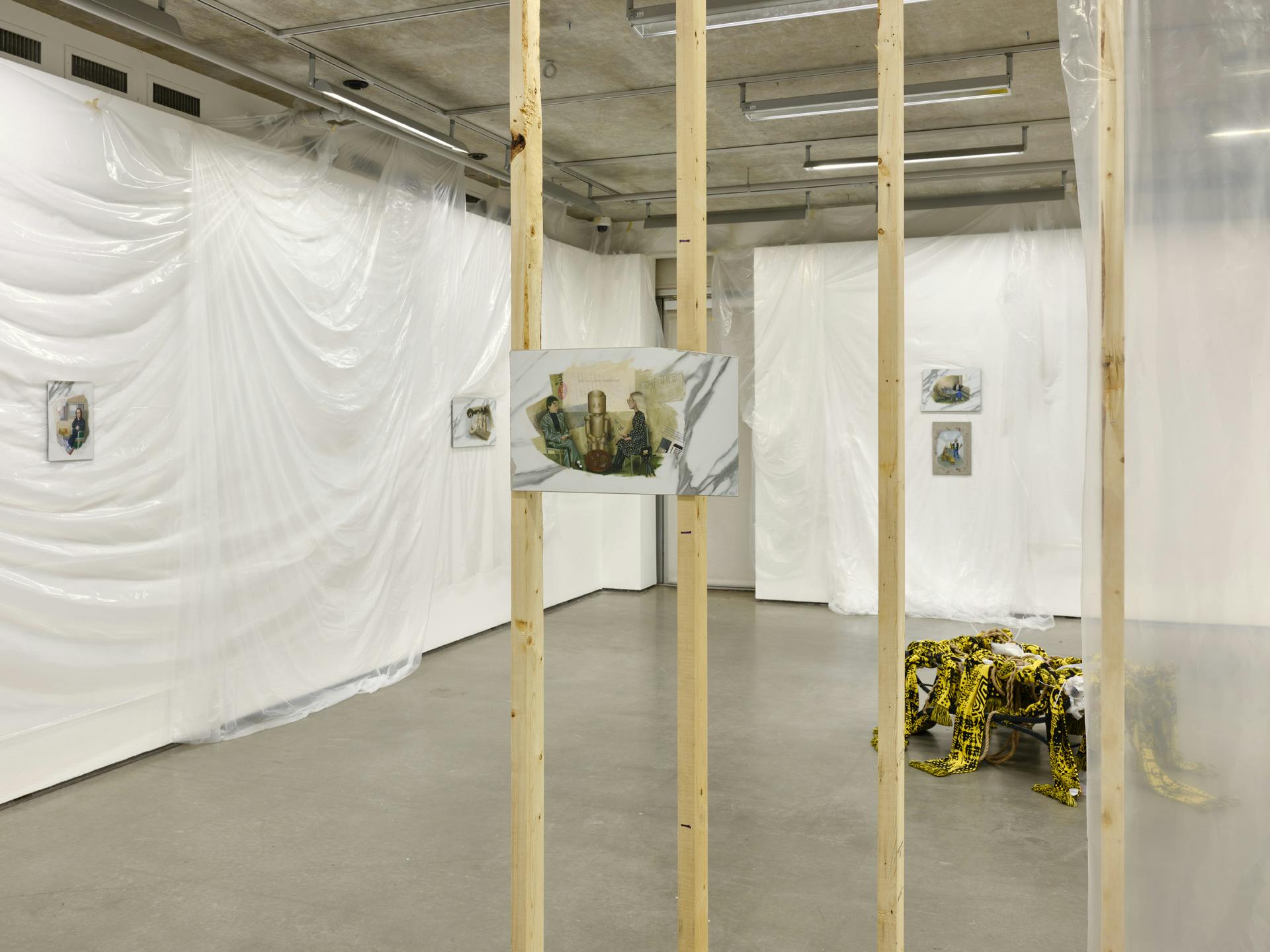 An unfinished wooden wall structure in a gallery space, on which hangs a painting on faux-marble tile. More paintings hanging on the gallery walls and a sculpture are visible through the wall structure. 