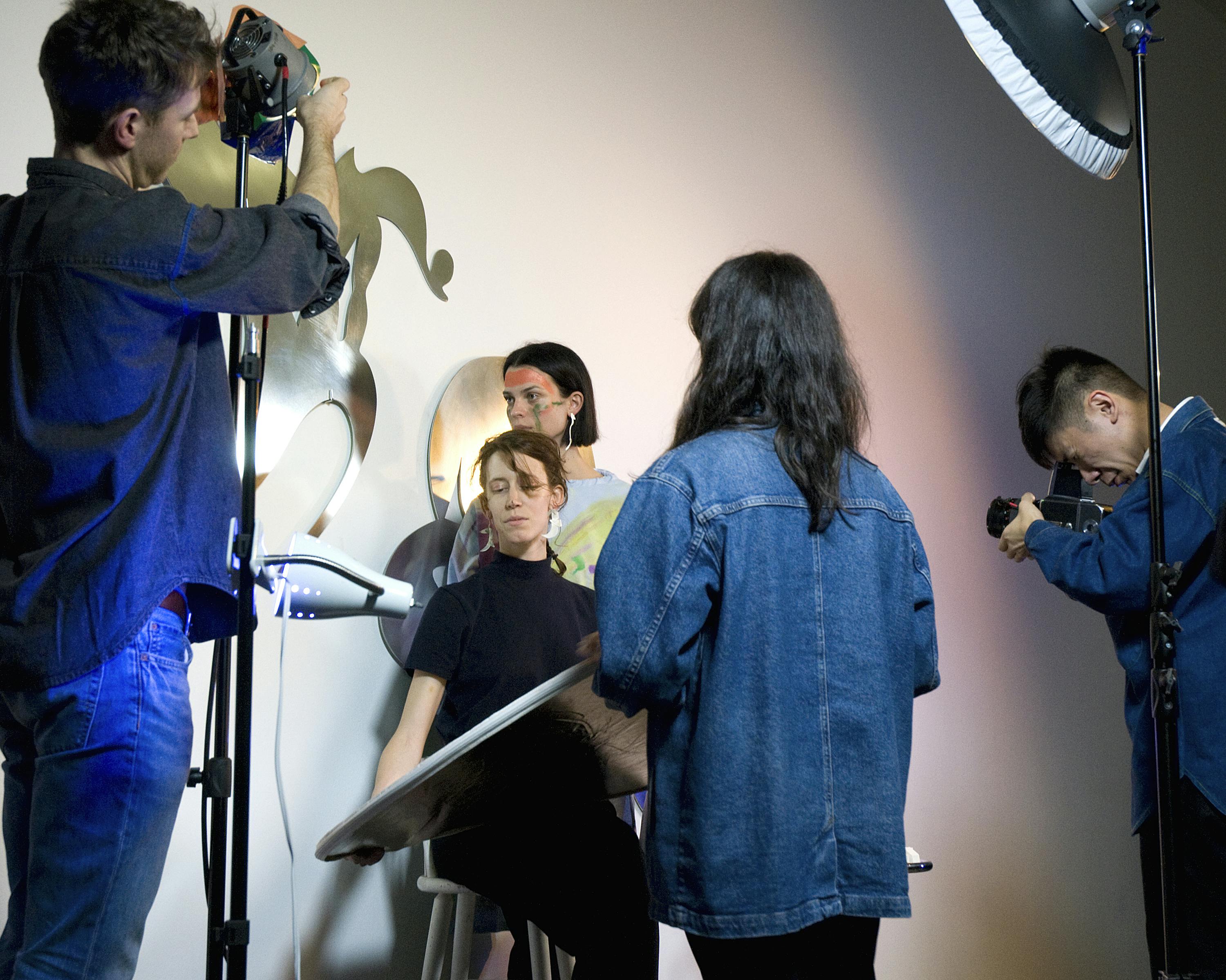 This is a close-up view of a performance taking place inside the gallery space. A man is adjusting the stage light, and another man taking a photograph of a seated woman in the middle.
