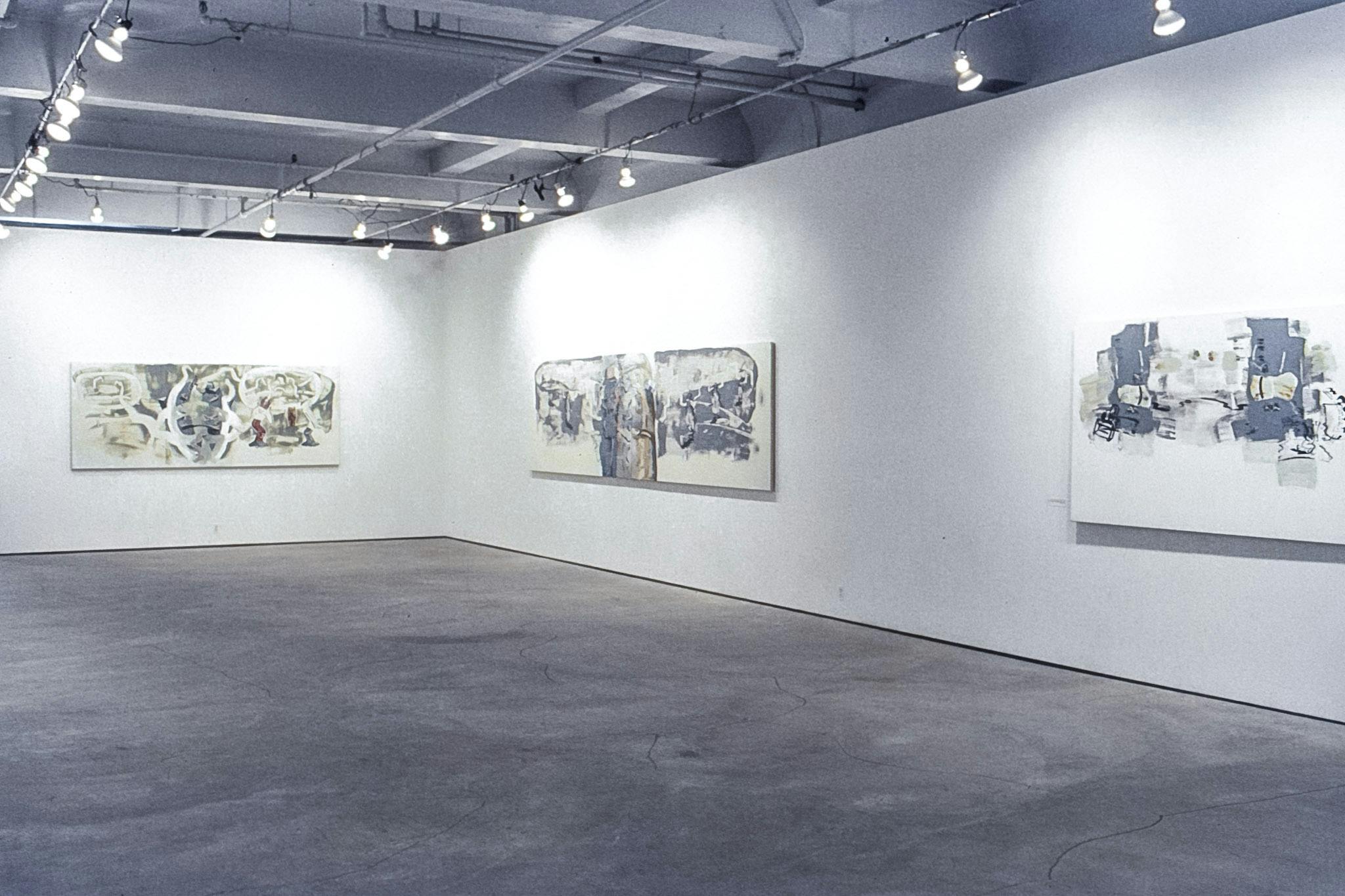 Three large abstract paintings mounted on the corner of a gallery space. These paintings are primarily white, with several layered details in grey, black, yellow, and red. 