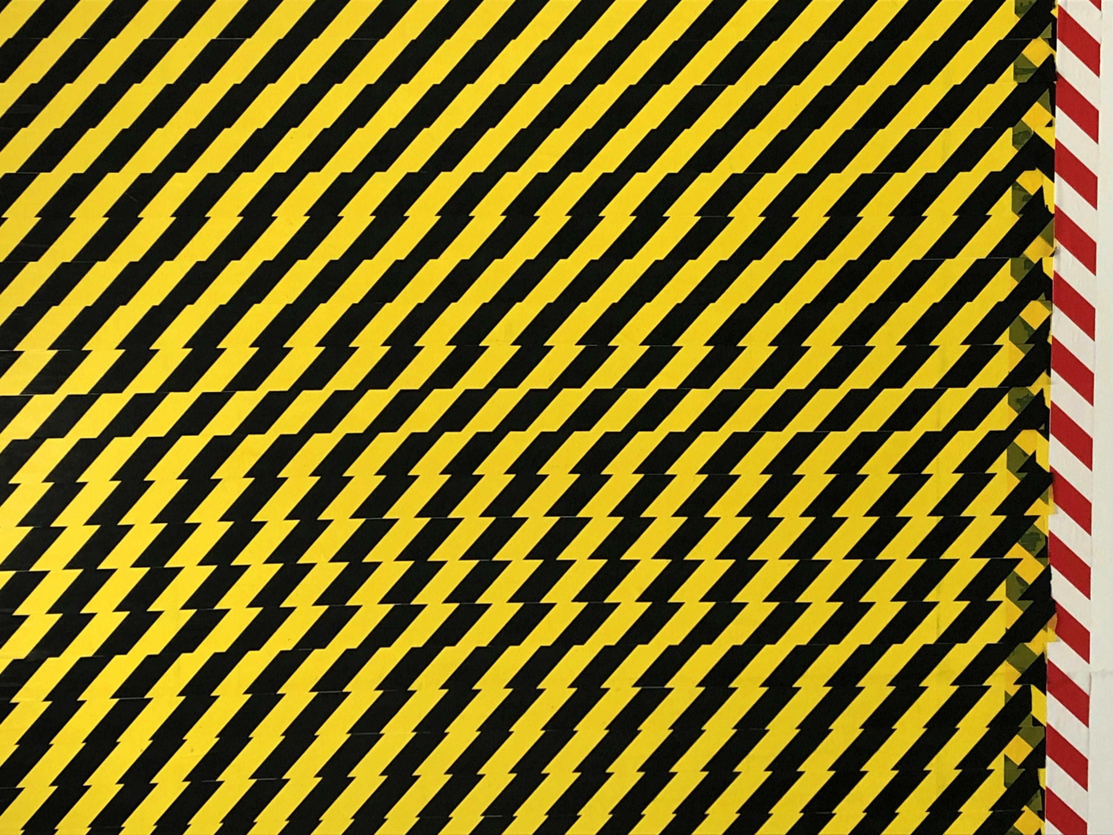 An image detail of black-and-yellow caution tape layered in horizontal striations. To the left, there is a single vertical strip of red-and-white caution tape.