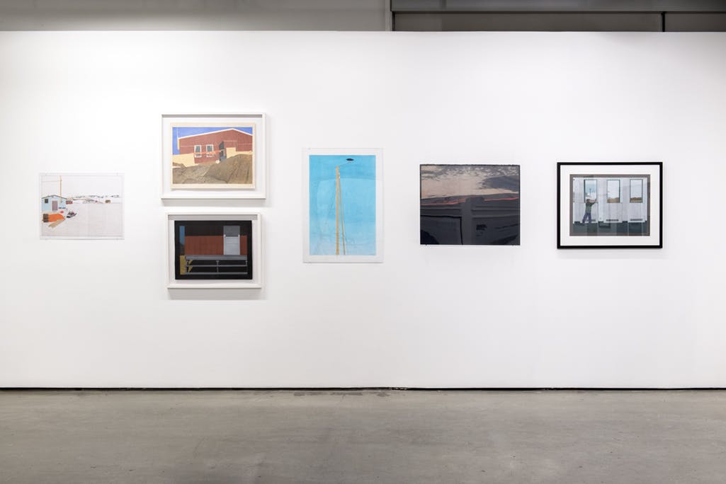 Multiple drawings by Itee Pootoogook hang on gallery walls. Six framed works are visible in this photograph. They depict built structures and natural landscapes. 