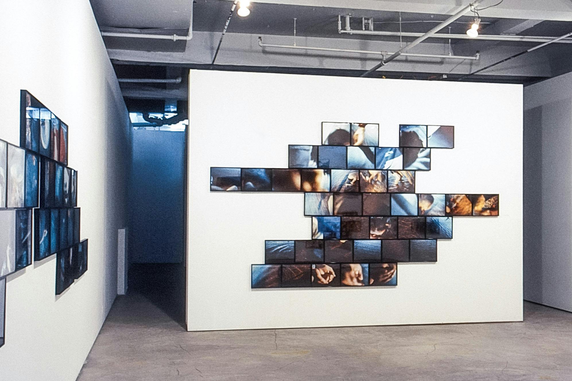 A gallery with a wall in the centre creating a division. This wall shows several photos of snippets of ripples on water and hands. The other visible wall has several photos as well, seen at an angle.