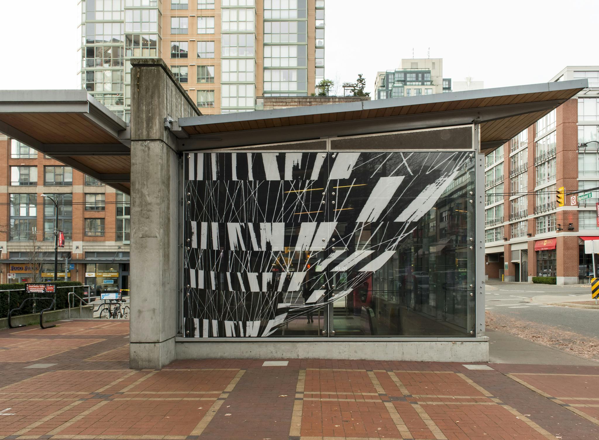 Image of the glass facade of the Yaletown-Roundhouse Station. The facade is installed with a vinyl print of a large-scale, black and white pattern resembling moving or folded fabric. 