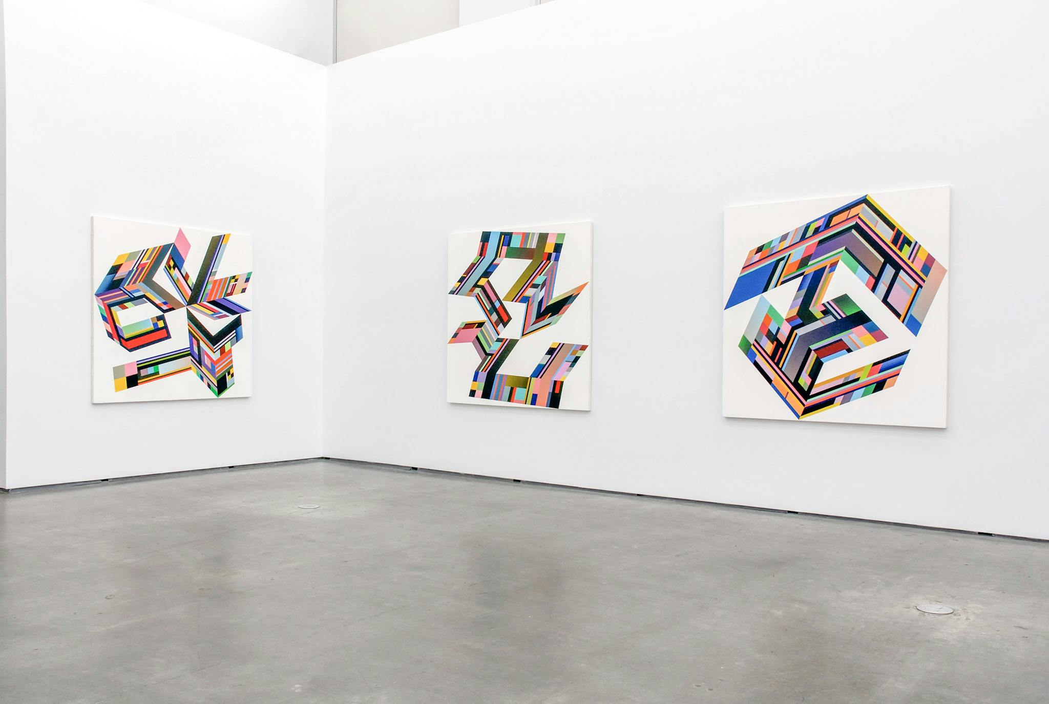 Three graphic designed works are mounted on the gallery walls. On each white canvas, an abstract shape is drawn with the combinations of various coloured cells.  