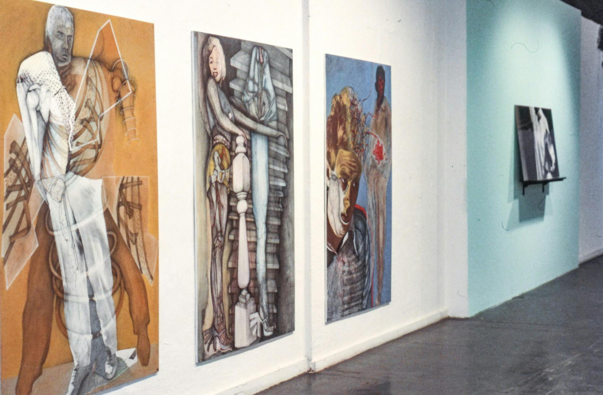 Three large paintings and a photo on the wall of a gallery. The paintings show Marlon Brando, Marilyn Monroe, and James Dean, each with anatomical drawings and mechanical images collaged on them.