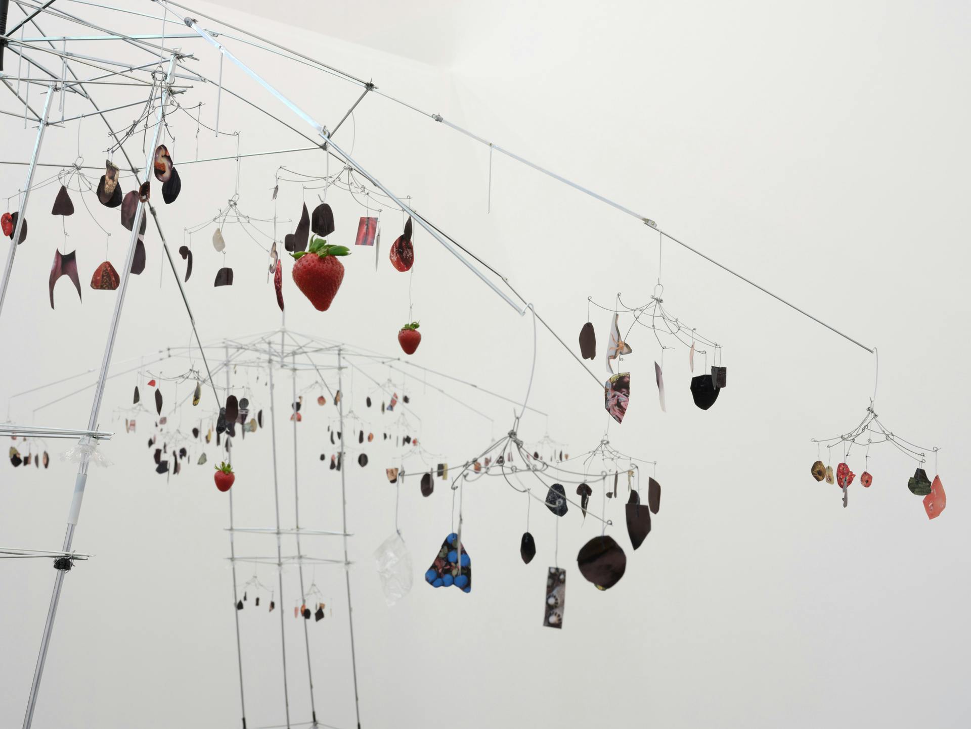 Paper cutouts and a strawberries hang from thin metal wires.