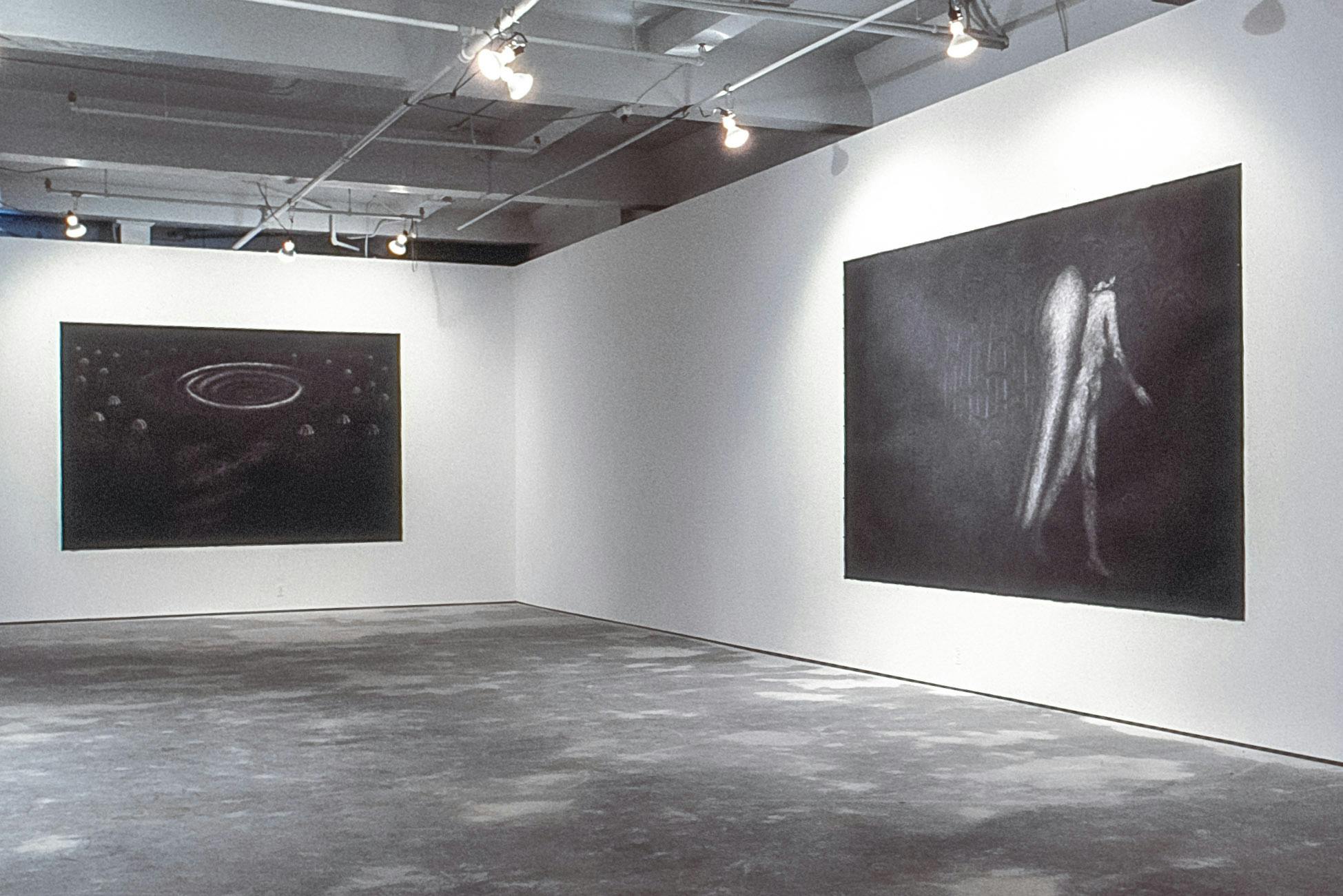 In the corner of a gallery, there are two large, dark charcoal drawings on the walls. One drawing shows a galaxy with planets and swirls. The other shows a nude angel walking, with their face turned.