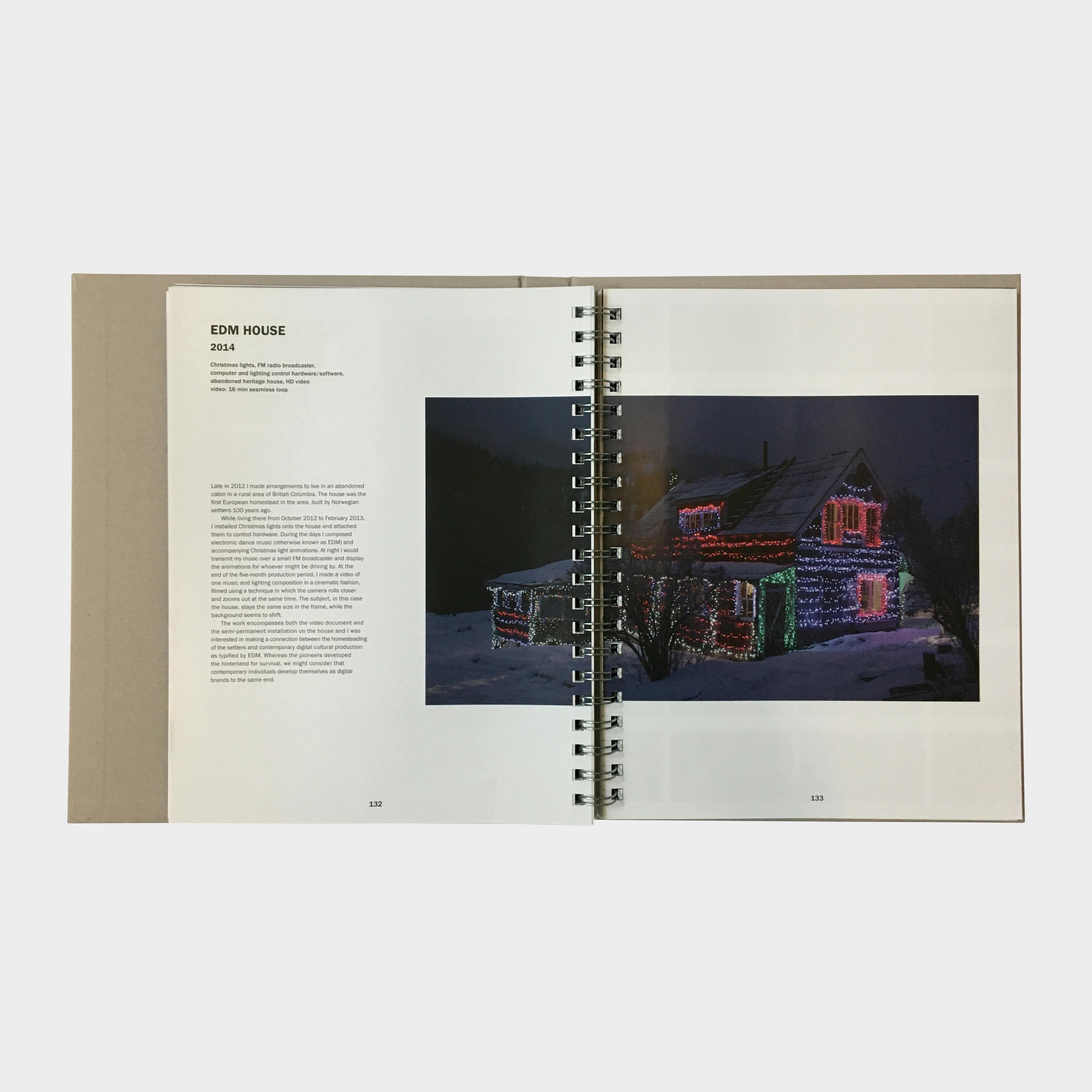 An image of an open page in Kevin Schmidt's monograph. The photograph printed on the page records the house decorated with holiday lights at night. 