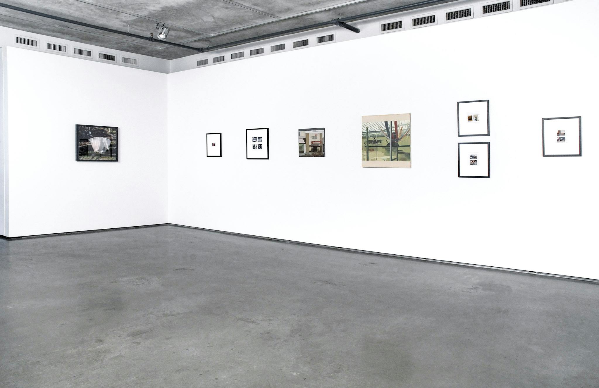 Various two-dimensional artworks are installed on the gallery walls. Some of them are small-sized photographs and others are paintings. They all depict urban landscapes. 